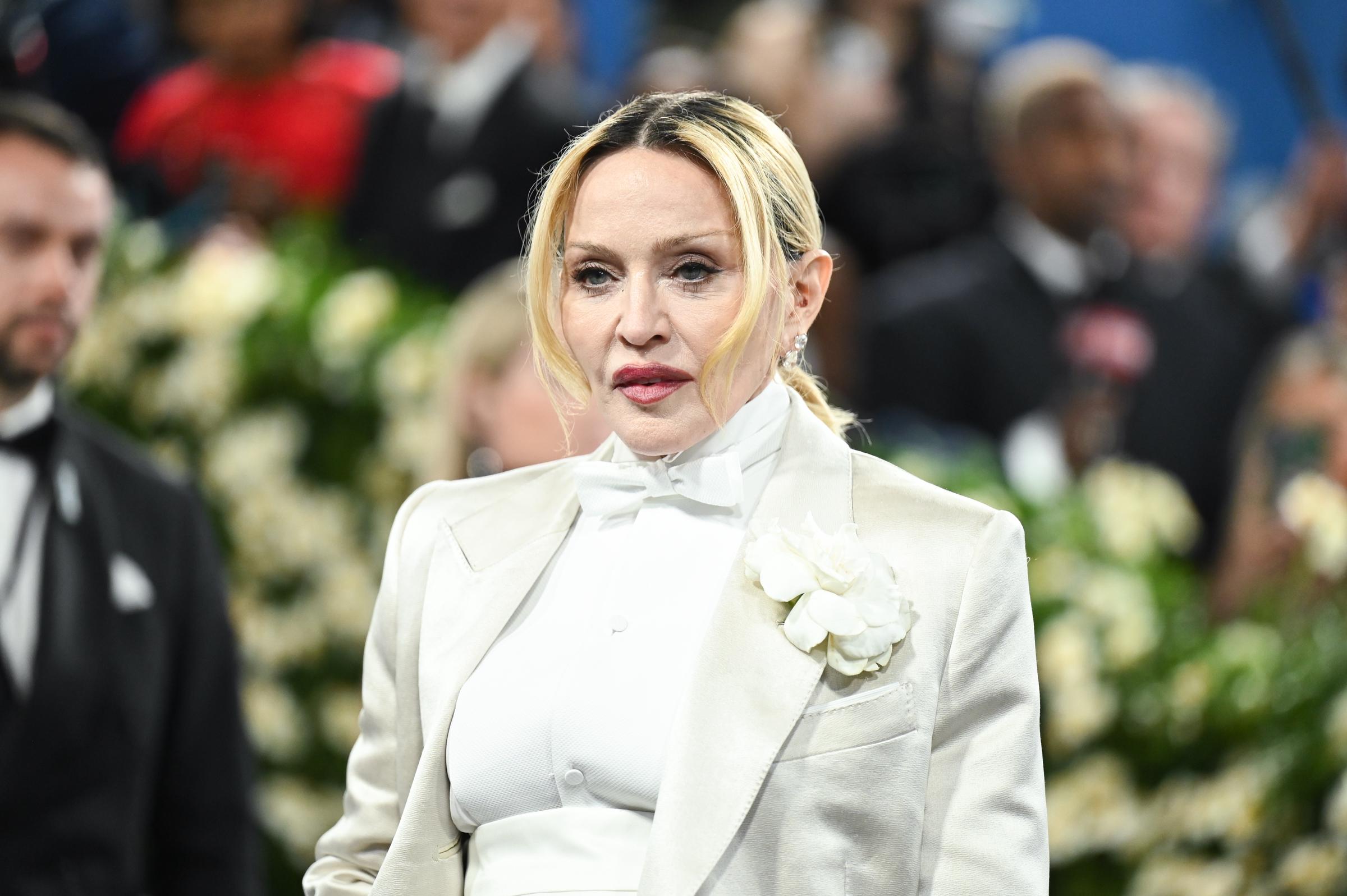 Madonna attends the 2025 Met Gala at the Metropolitan Museum of Art in New York City on May 5. She arrived in an all-white tailored look featuring a high-neck shirt, bow tie, structured jacket, and floral detail. | Source: Getty Images