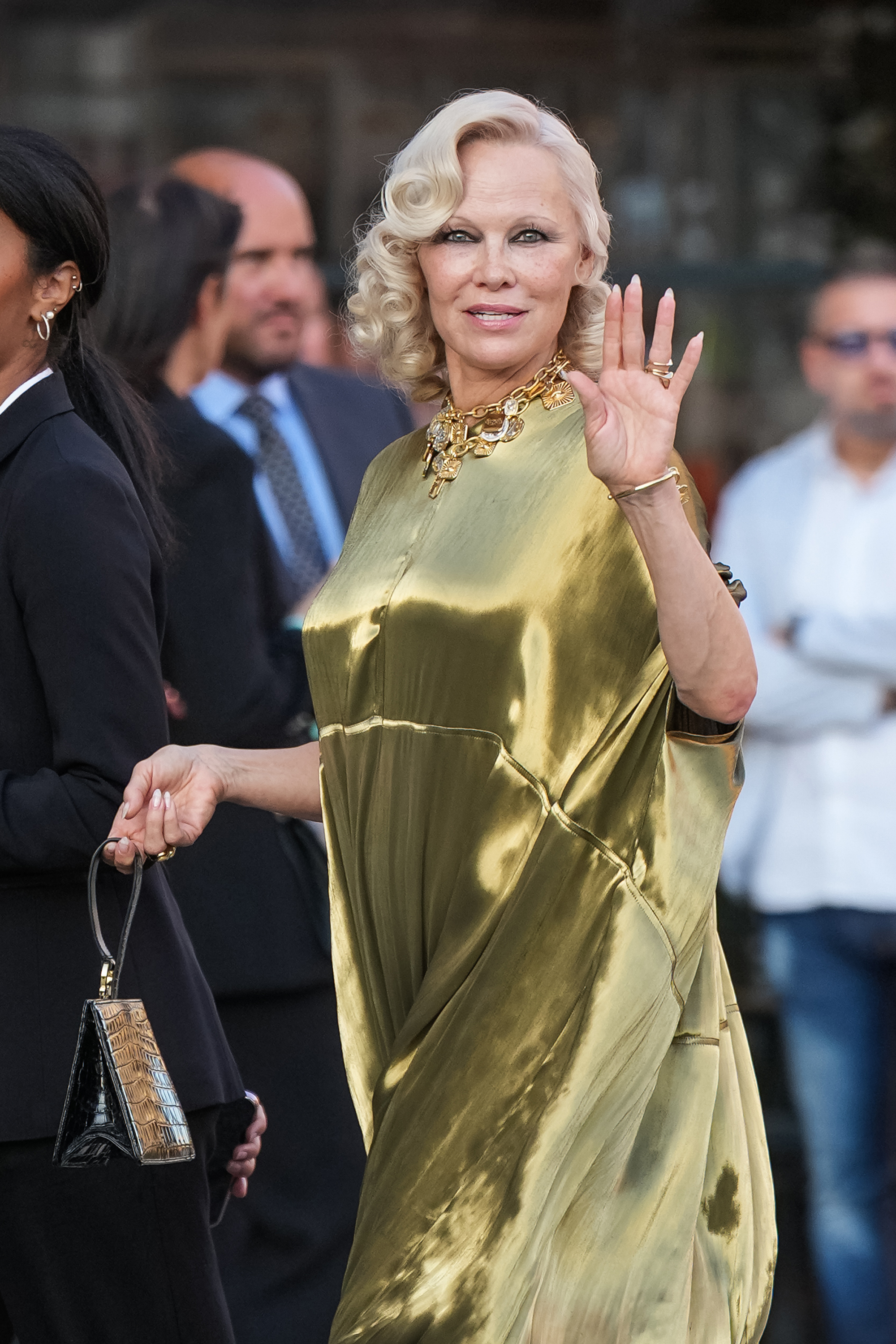 A closer view of Anderson highlights her platinum-blonde curls, gold statement necklace and dark eye makeup as she waves to onlookers in Milan. The actress was photographed arriving during Milan Fashion Week on September 22, 2026. | Source: Getty Images