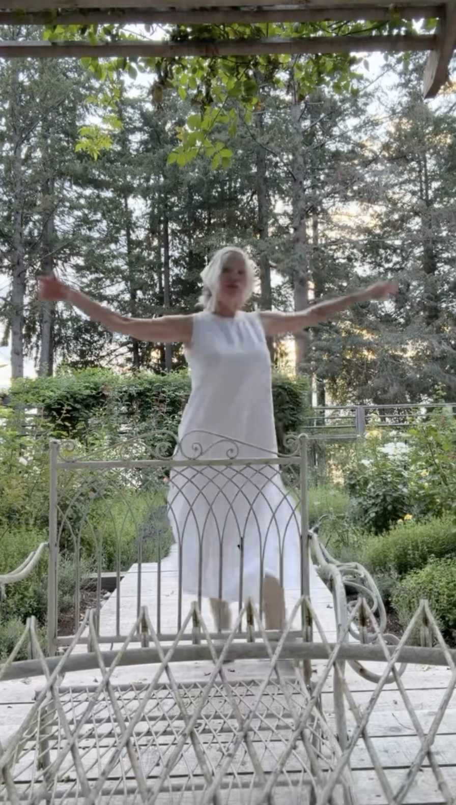 Pamela Anderson spins freely with her arms outstretched across the wooden deck of her Arcady garden, perfectly embracing her personal philosophy to "live romantically wherever you are." Wearing a breezy, sleeveless white midi dress against a lush backdrop of evergreens and garden greenery, she captures the uninhibited peace and self-made romance that define her quiet life on Vancouver Island. | Source: Instagram/pamelaanderson