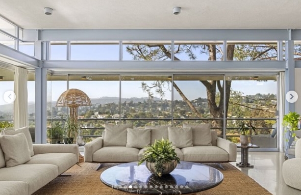 Expansive windows frame sweeping hillside views from the living room, where neutral sofas surround a reflective oval coffee table. Natural light fills the understated space, while the home's elevated Los Feliz setting becomes part of the decor, offering an unobstructed outlook across the surrounding Los Angeles landscape. | Source: Instagram/jparkerstanton