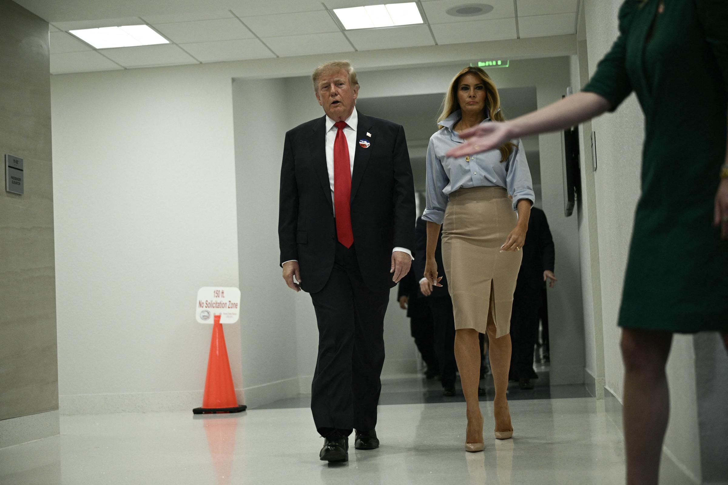 Making their way down an interior hallway after casting their votes, the First Lady commands attention in her rolled-sleeve collared top and front-slit skirt, anchoring the relaxed palette with vertiginous nude stilettos that provide a daring, razor-sharp edge to every step.