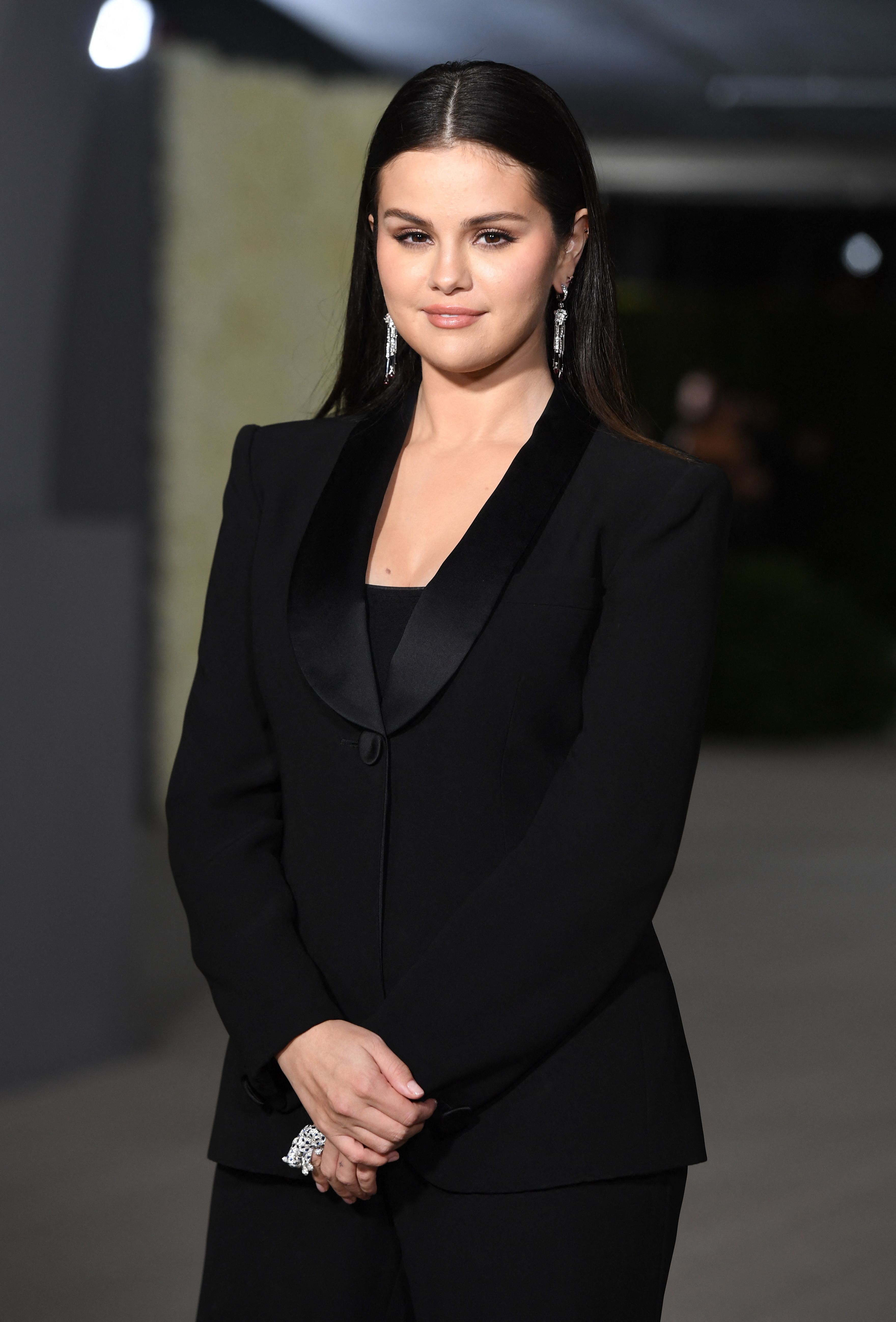 Back in a suit, this time a sleek black one with an embellished neckline, Selena Gomez strikes a poised, businesslike pose with her hands held in front as she attends the 2nd Annual Academy Museum Gala at the Academy Museum of Motion Pictures in Los Angeles.