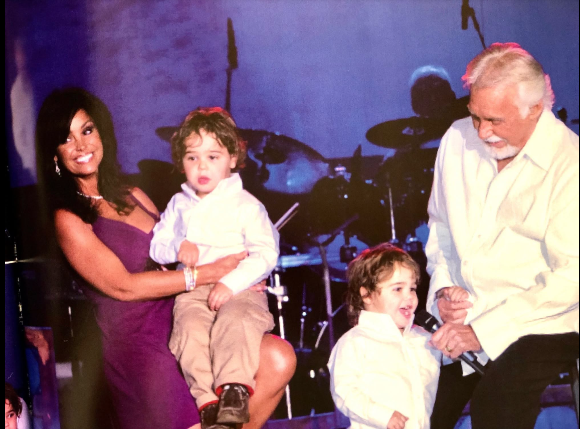 The early family photo shows Kenny Rogers and Wanda Miller sharing the stage with their young twin sons, Justin and Jordan, offering a glimpse of the boys years before their grown-up appearance sparked a lively debate over who they resemble. | Source: Facebook/Kenny Rogers