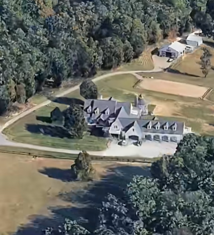 The large country residence features several connected sections, steep rooflines, and dormer windows. The driveway and surrounding lawns show how the house sits within the property's open landscape. | Source: Youtube/HouseOfCelebs