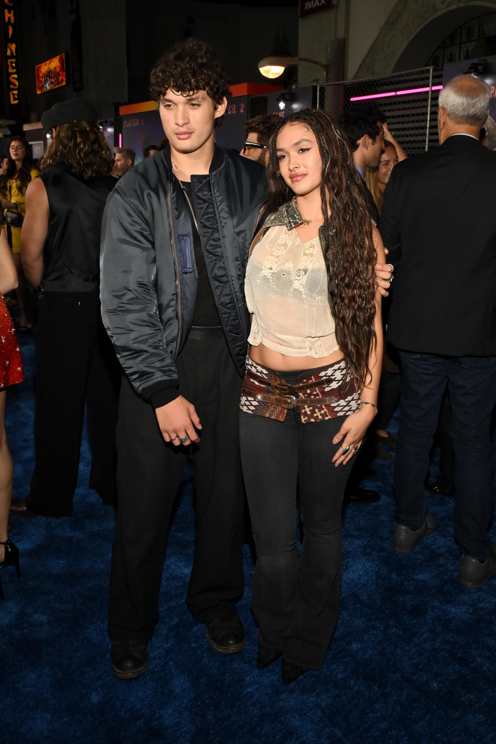Nakoa-Wolf Momoa and Lola Iolani Momoa pose full-length together on the blue carpet at the Los Angeles premiere of Paramount Pictures' "Street Fighter" at the TCL Chinese Theatre on October 12, 2026, in Hollywood, California. Showing off their complementary premiere looks, Nakoa-Wolf stands tall with an arm around his sister while clad in black boots, trousers, and a bomber jacket, as Lola styles pointed black shoes beneath her flared jeans, paired with a sheer sleeveless top and an intricately patterned waist wrap. | Source: Getty Images