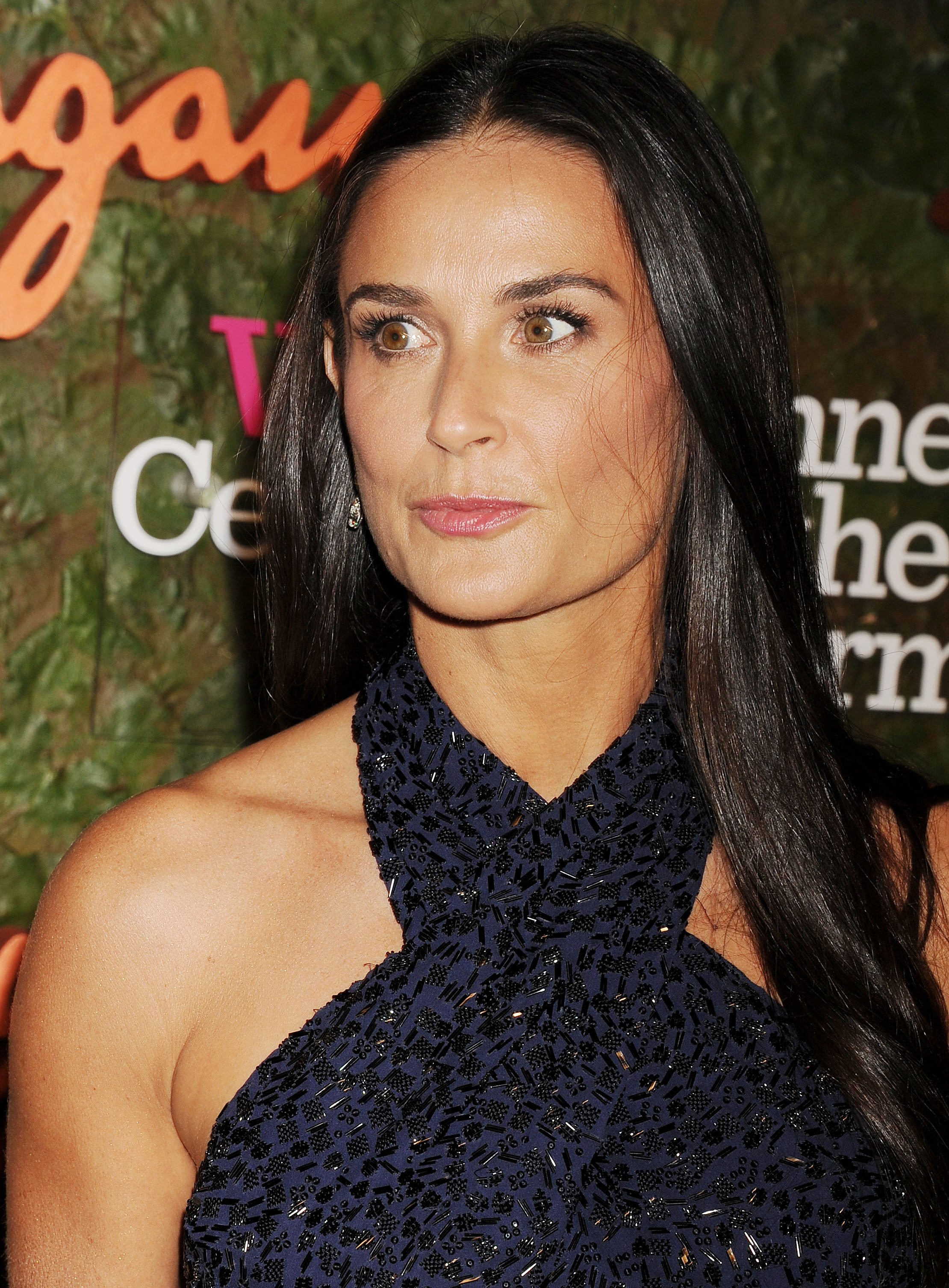 Bathed in warm light, Demi Moore exudes quiet strength and refined allure, her gaze both poised and enigmatic. Her intricate navy gown shimmers softly, echoing her understated elegance.