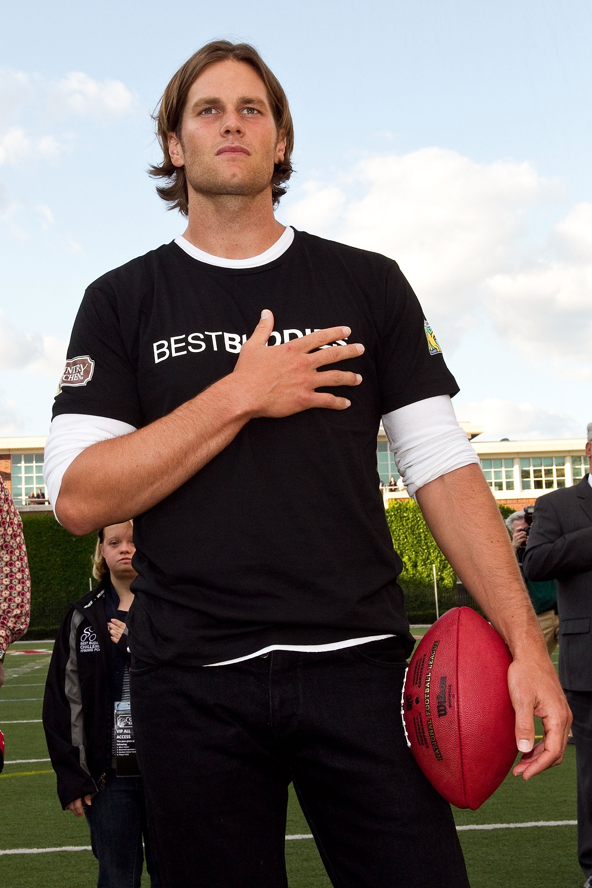 With one hand over his heart and the other clutching a football, Tom Brady stands in solemn reflection during the U.S. National Anthem at the Audi Best Buddies Challenge flag football kickoff at Harvard Stadium in Boston.