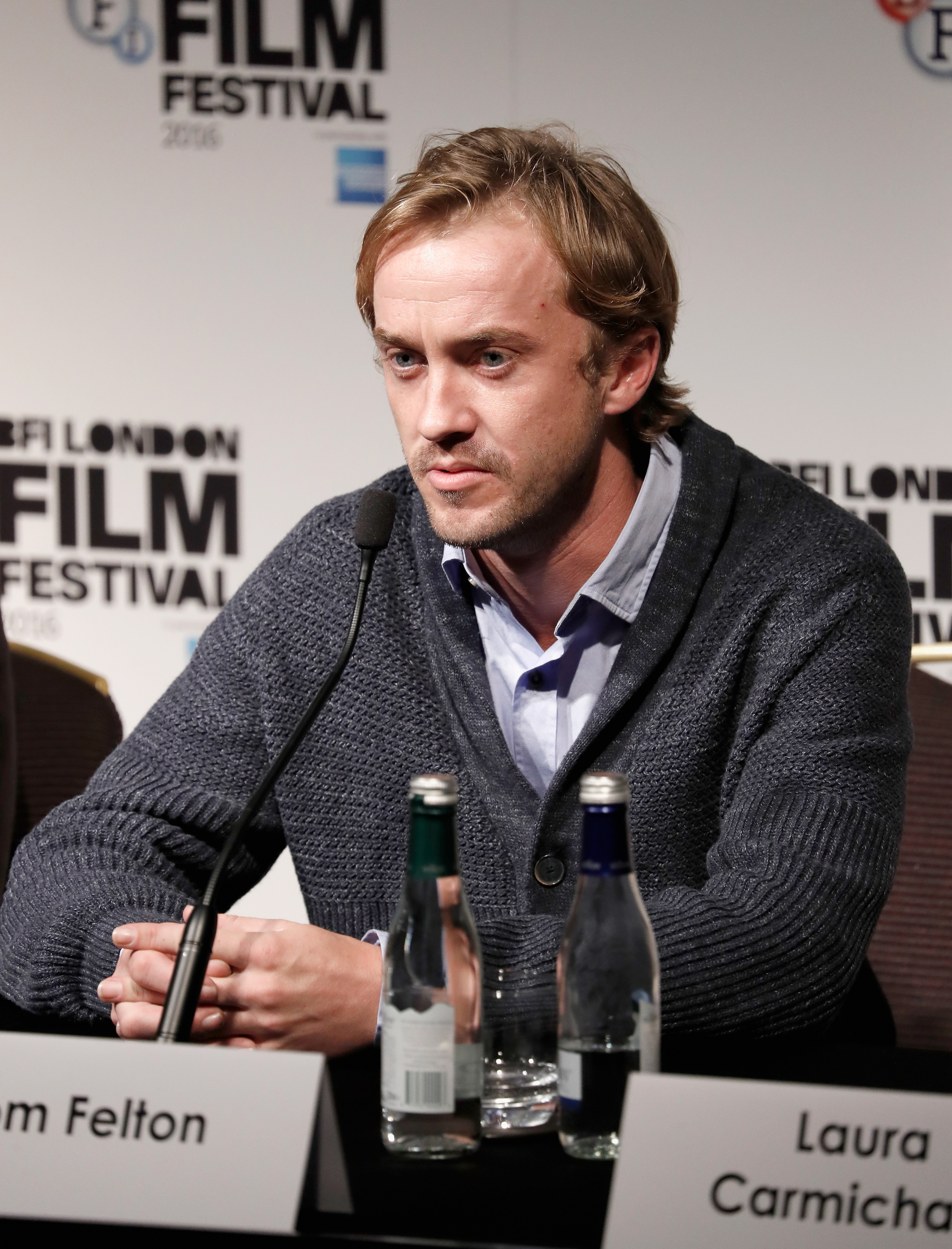 Tom Felton sits poised at the press table, his thoughtful expression matching the weight of the conversation at hand. Wrapped in a textured sweater, he brings a calm, grounded presence to the room of eager listeners. At the "A United Kingdom" press conference during the 60th BFI London Film Festival, his quiet focus speaks louder than words.
