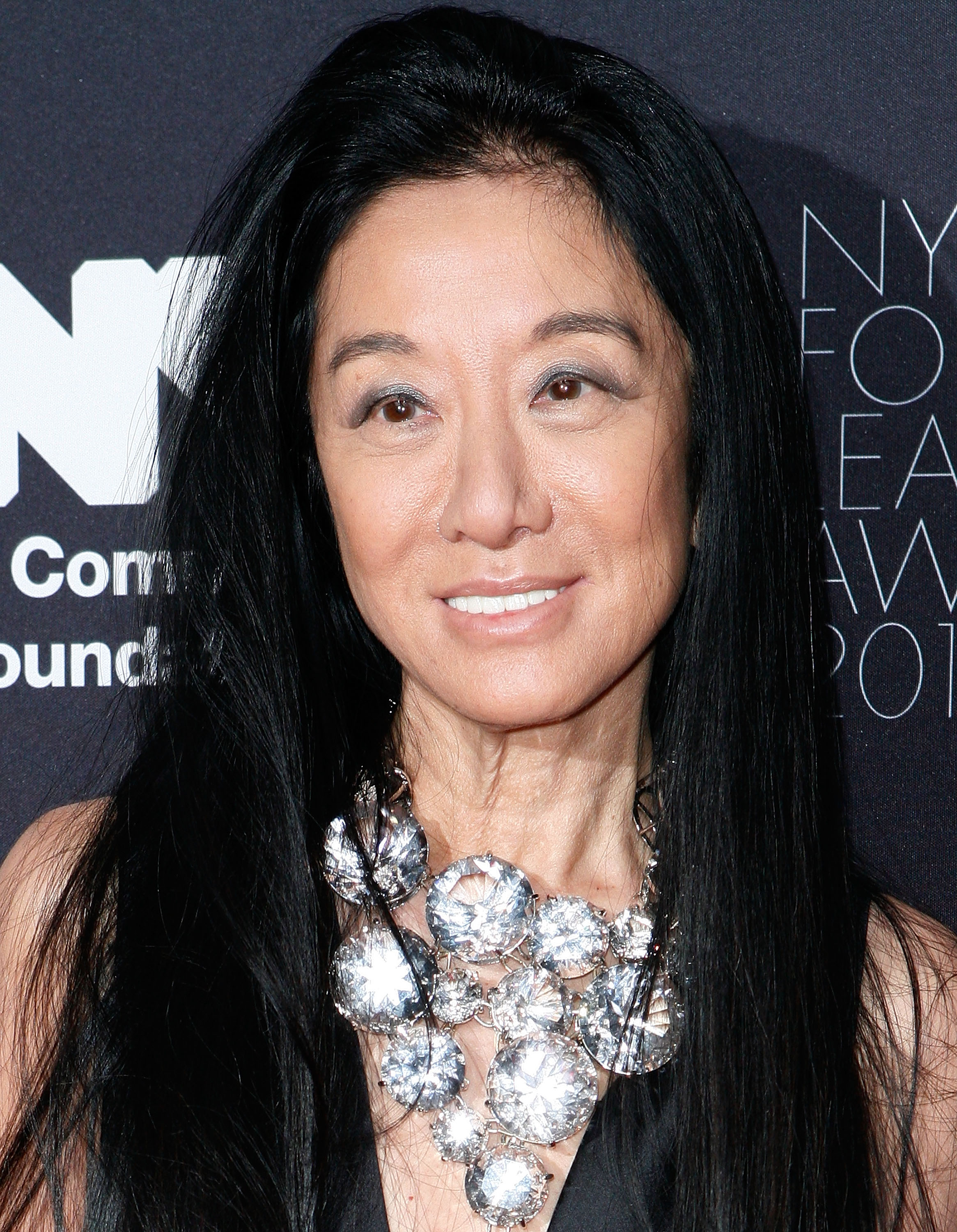 Vera Wang arrived with a radiant smile at the NYC & Company Foundation Leadership Awards Gala held at The Plaza Hotel on December 1, 2010, in New York City. The celebrated designer highlighted her black evening attire with an opulent bib necklace composed of oversized, multifaceted crystal discs, framing her features beneath voluminous, flowing black hair and shimmering silver eye makeup. | Source: Getty Images