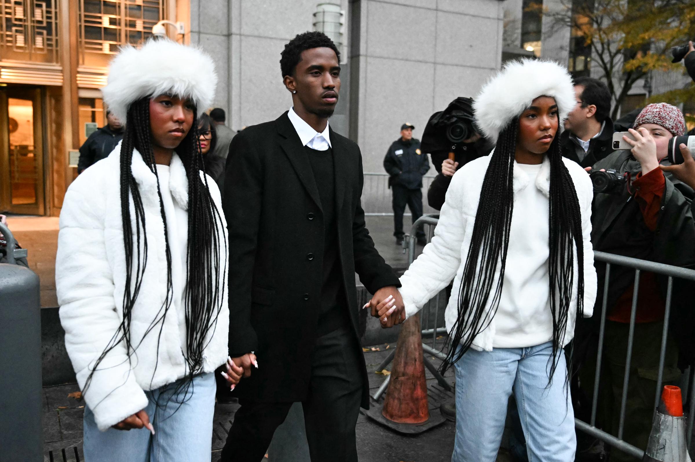 King walks hand in hand with his twin sisters, Jessie and D’Lila Combs, as they leave a courthouse in somber black and winter-white outfits. Surrounded by cameras, they move forward together in a quiet show of unity and support.