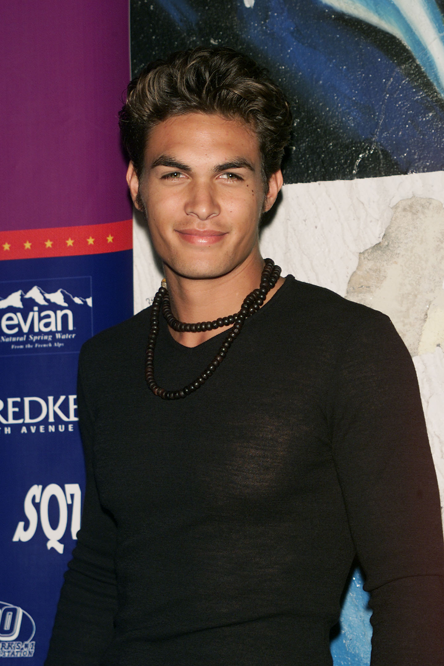 Jason Momoa from "Baywatch Hawaii" smiles upon arriving at Seventeen Magazine's 8th Annual Teen Party at Roseland Ballroom on October 27, 2000, in New York City. Sporting short, wavy brown hair, a clean-shaven look, and a dark beaded necklace over a long-sleeved black V-neck shirt, the young actor poses before the event sponsor wall. | Source: Getty Images