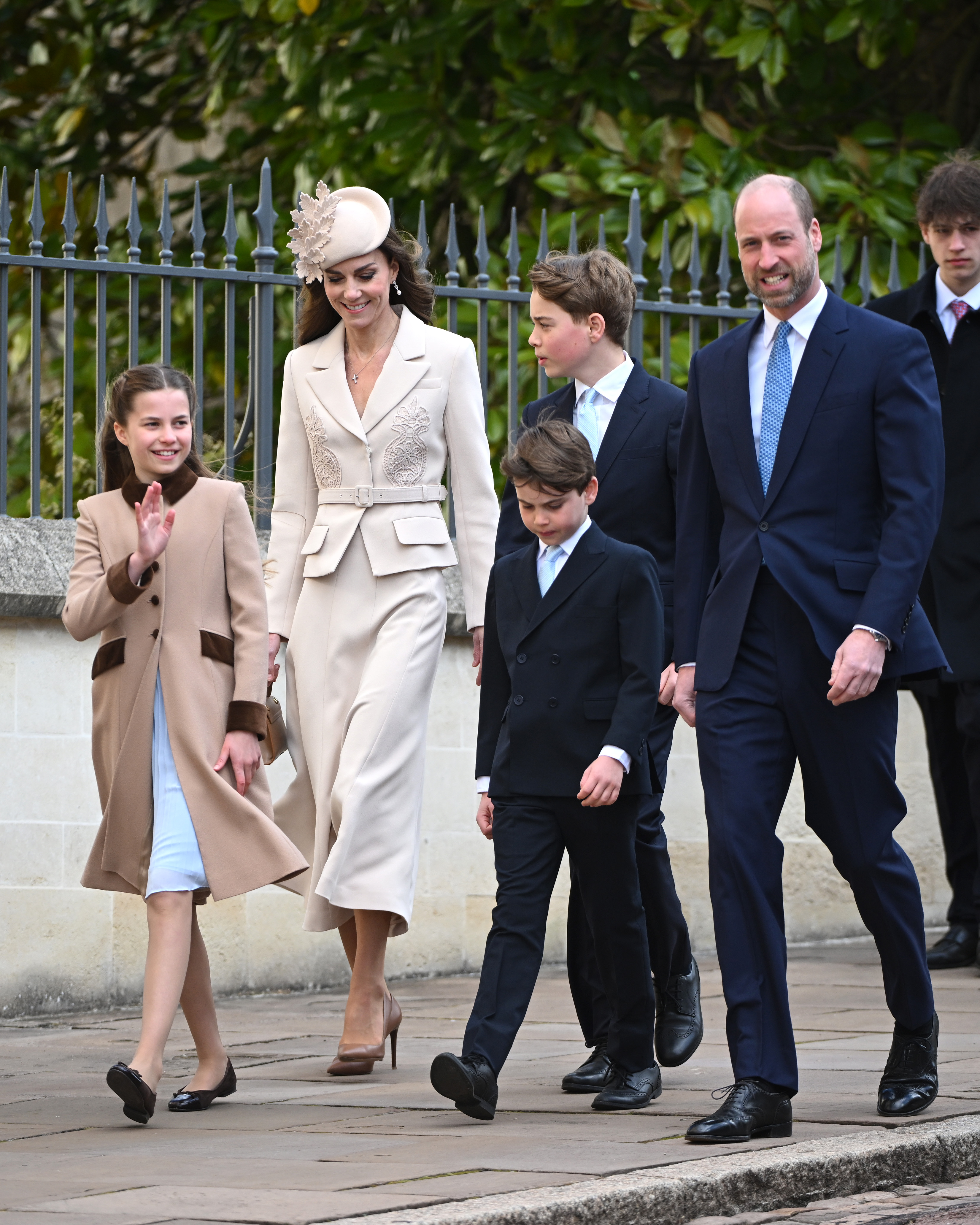 The full Wales family together in one frame as they make their way towards St George's Chapel on Easter Sunday, each of the five caught mid-stride in the April light. Princess Charlotte waves to the crowds on the left while Prince Louis walks between his parents, and Prince George, already towering above his younger brother, is visible just behind the Princess of Wales. | Source: Getty Images