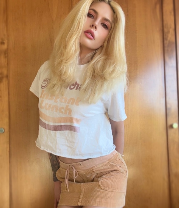 Posing casually against a warm wooden panel wall, Cleo Rose Elliott served effortless retro style in an Instagram upload from March 22, 2025. Her playful look teamed a cropped white Maruchan Instant Lunch tee with a drawstring tan corduroy mini skirt, while her voluminous blonde layers fell softly past her shoulders.