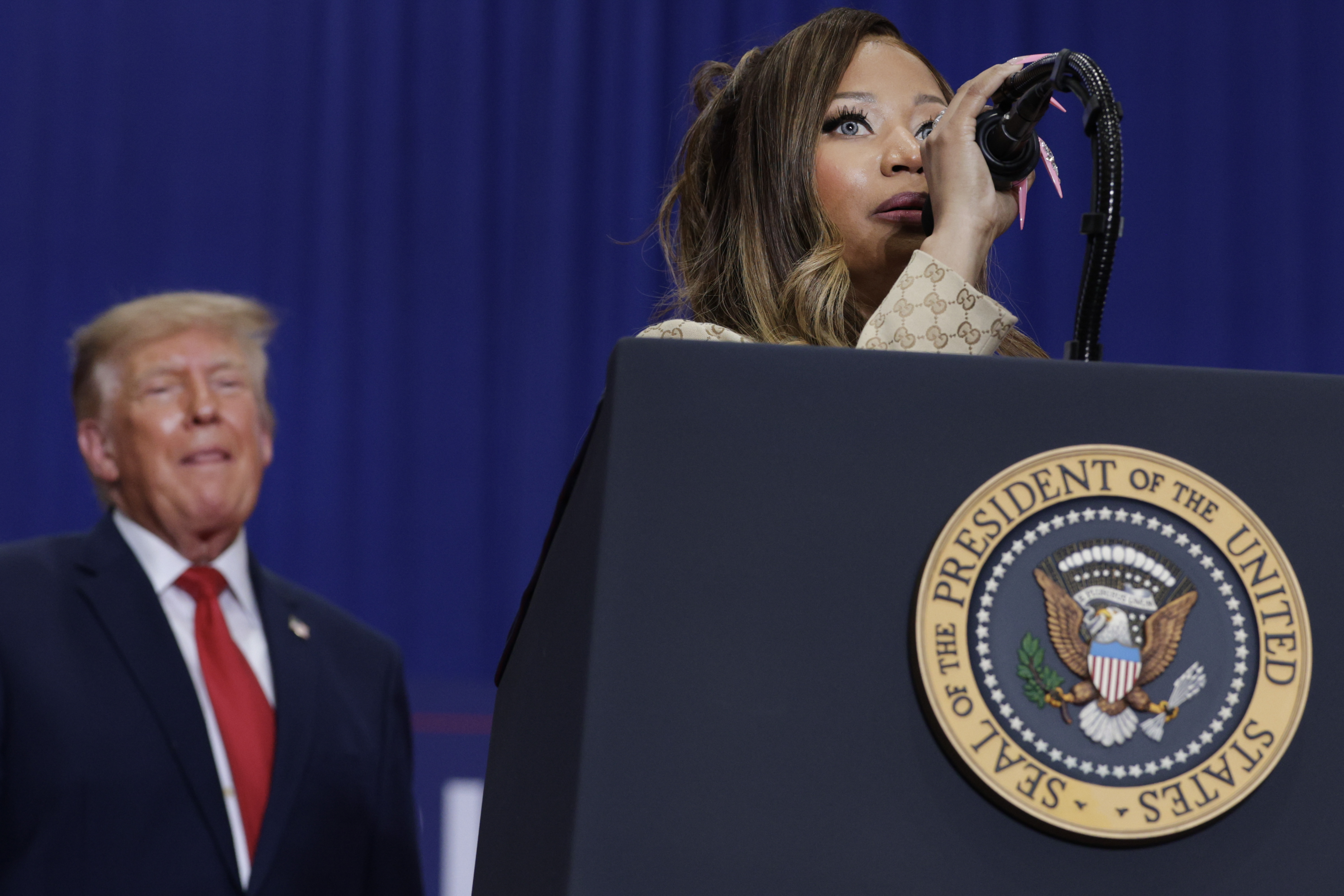 Nicki Minaj speaks from behind a lectern bearing the presidential seal while Donald Trump watches from the side — a rare moment in which the rapper takes center stage at a presidential rally rather than a concert. | Source: Getty Images