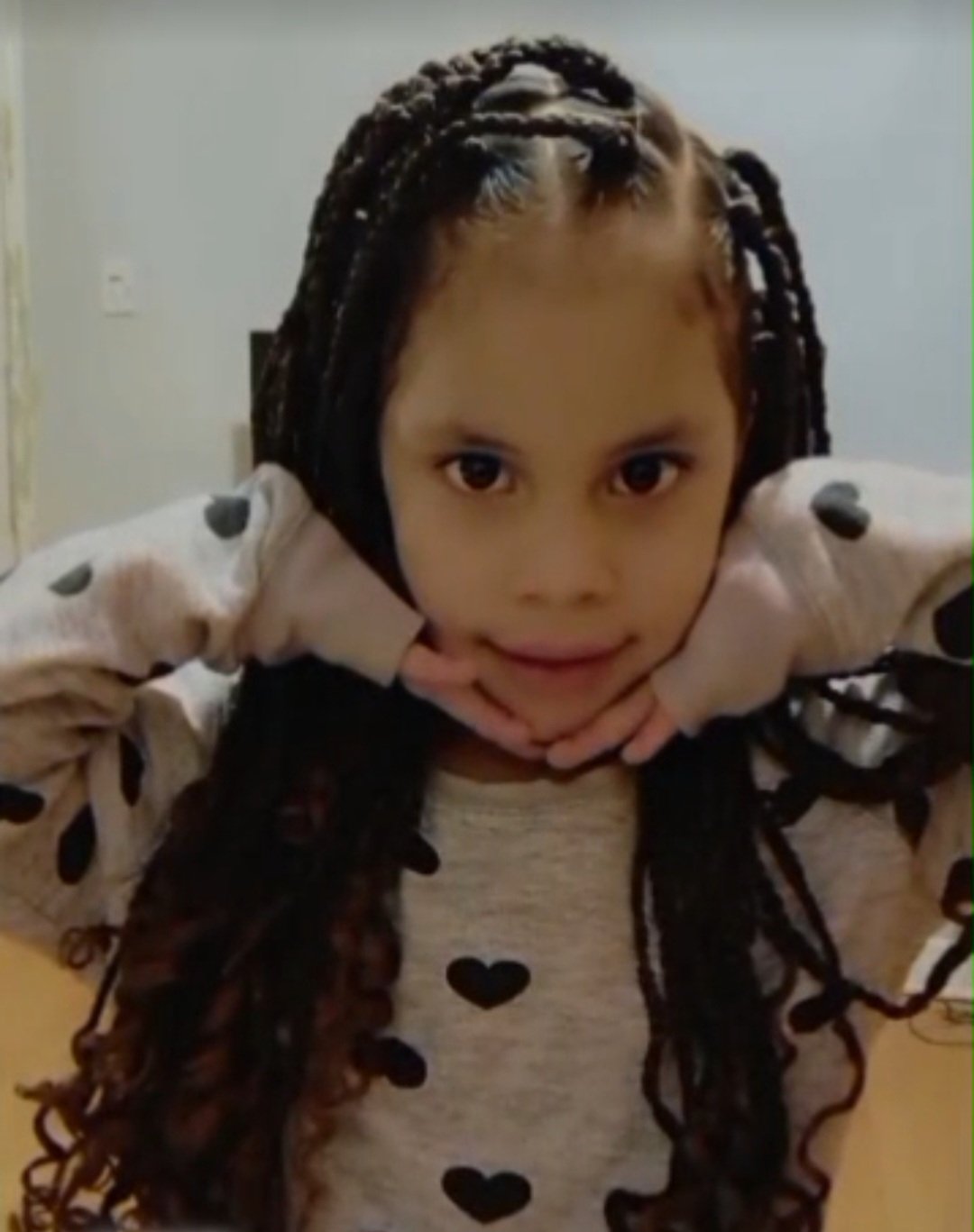 Eddimar Paola Hernández Chacón struck a sweet pose while framing her chin between both hands inside her long-sleeve cuffs. She wore her dark hair styled in long braids with curled ends, dressed in a cozy heather-grey top adorned with black heart prints. | Source: GoFundMe