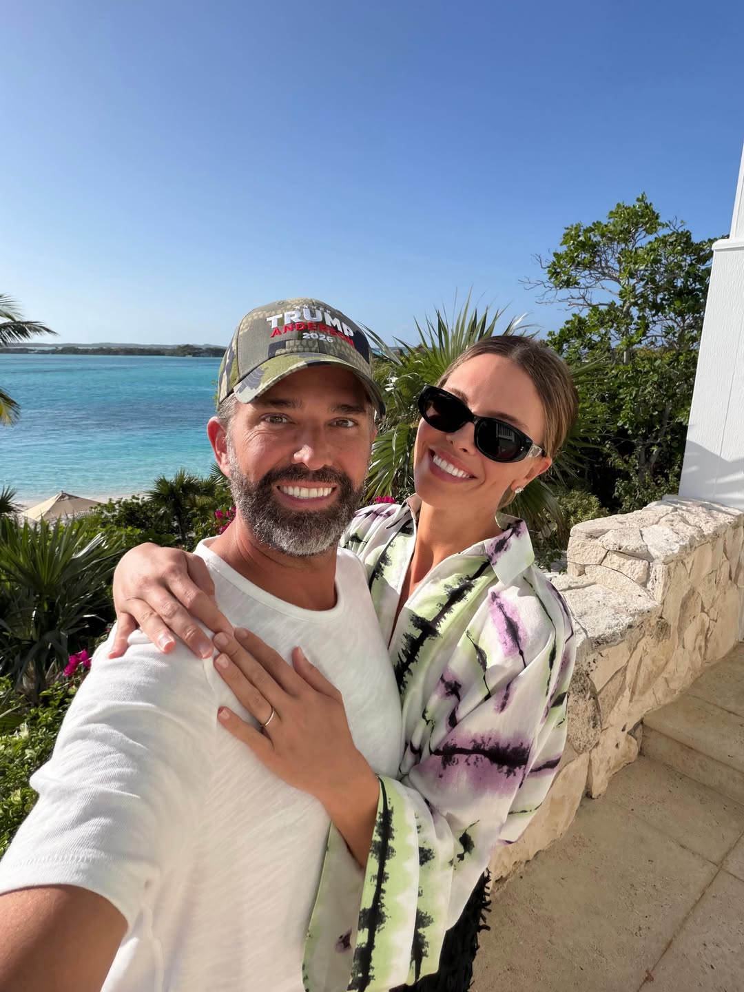 Donald Trump Jr. and Bettina Anderson smile for the camera from a sunlit terrace overlooking the Caribbean, with Anderson’s wedding band visible on her hand. | Source: Instagram/bettinatrump