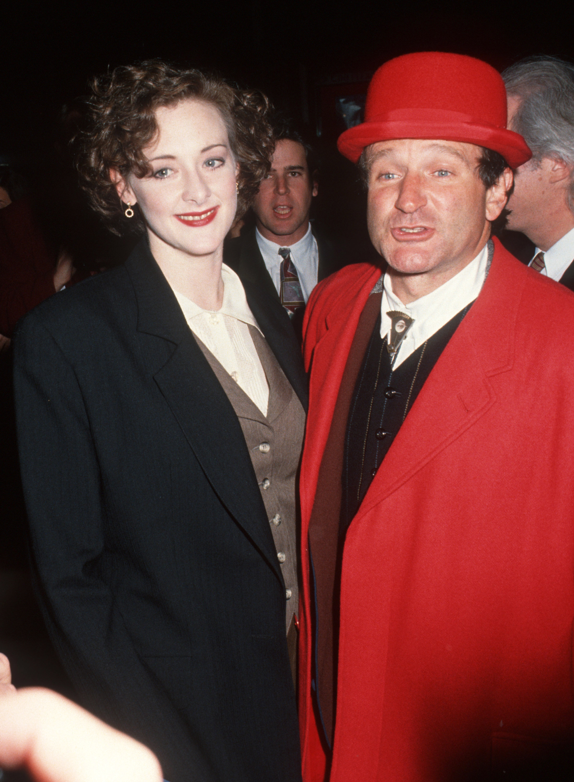 Joan Cusack stands beside Robin Williams, whose bold red outfit steals attention at first glance. Meanwhile, her tailored layered look and classic smile add effortless elegance.