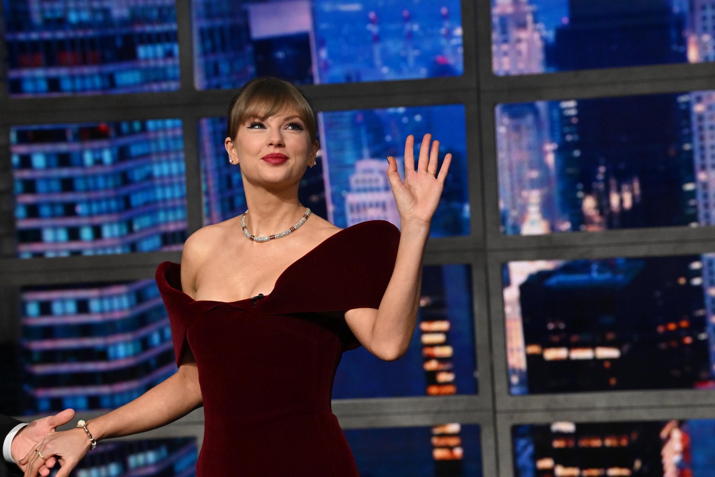 Taylor Swift waves to the audience while stepping onto the stage of "The Late Show with Stephen Colbert," wearing a burgundy, off-shoulder David Koma minidress that accentuated her silhouette and drew widespread attention online.