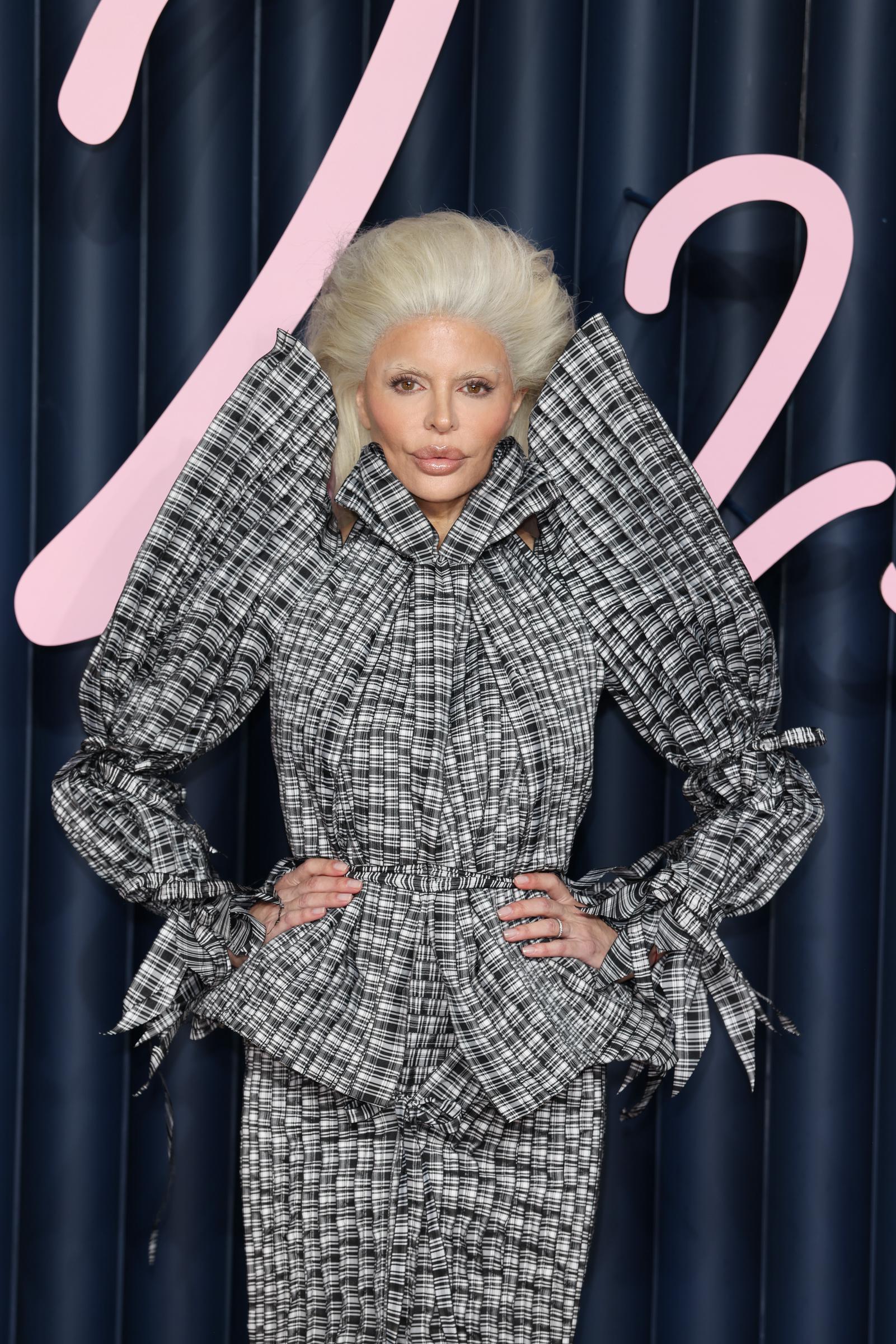 Lisa Rinna makes a striking appearance in a dramatic black-and-white plaid ensemble with exaggerated sleeves and sculptural detailing. Her towering platinum-blonde hairstyle and bleached eyebrows create a futuristic look, far removed from her signature brunette layers. | Source: Getty Images.