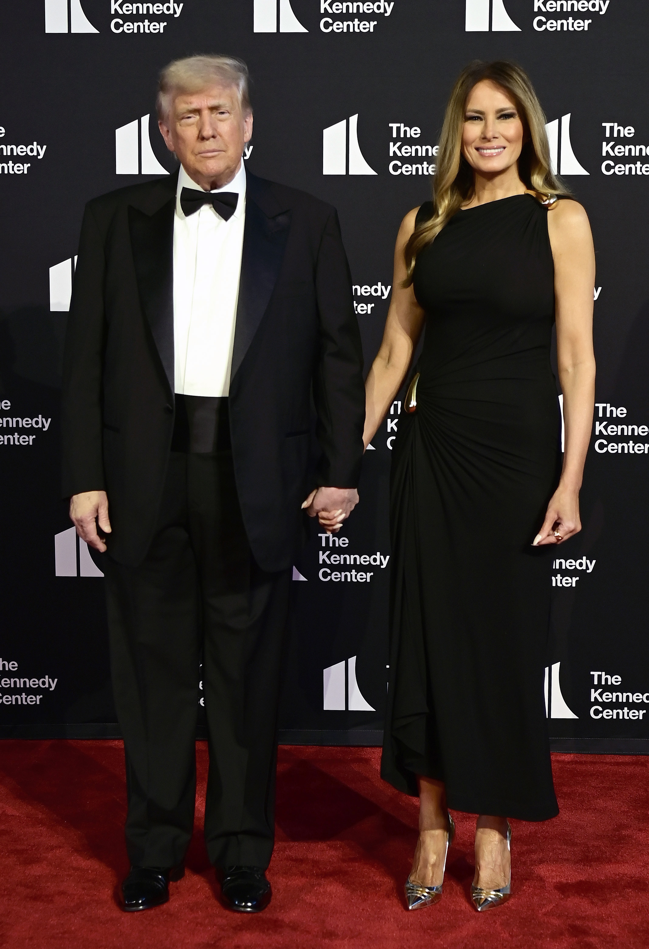 Framed by the Kennedy Center backdrop, the president maintains a solemn pose as the first lady smiles beside him during their red carpet appearance on June 11, 2025.