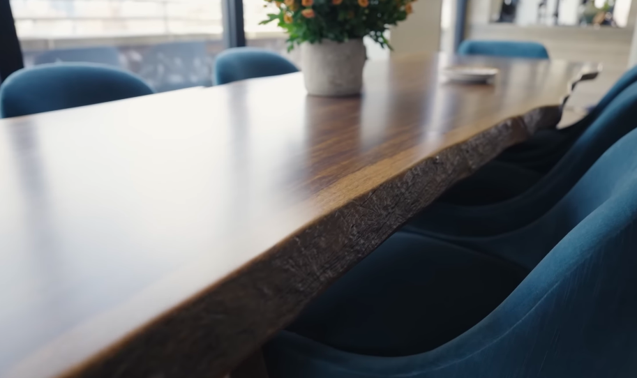 A close-up reveals the table's beautifully uneven live edge, preserving the character of the original wood. That raw texture is exactly the kind of imperfection the couple uses to soften the apartment's contemporary architecture. | Source: YouTube/Architectural Digest