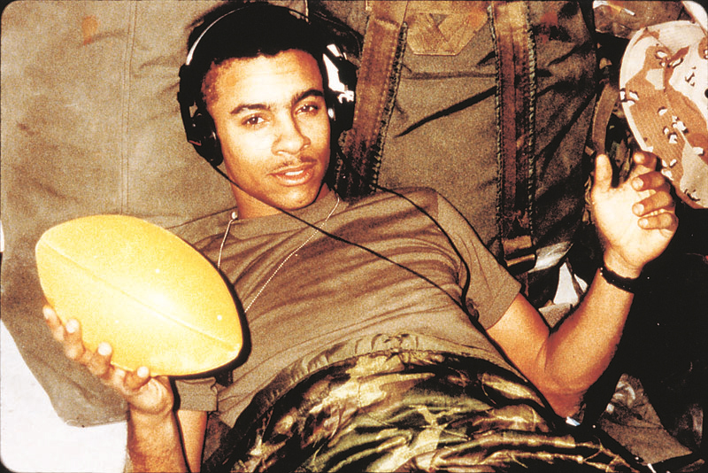 Shaggy reclines on a military cot wearing headphones, resting one arm beside him while holding a football | Source: Courtesy of Orville Richard Burrell, aka Shaggy | US Department of War