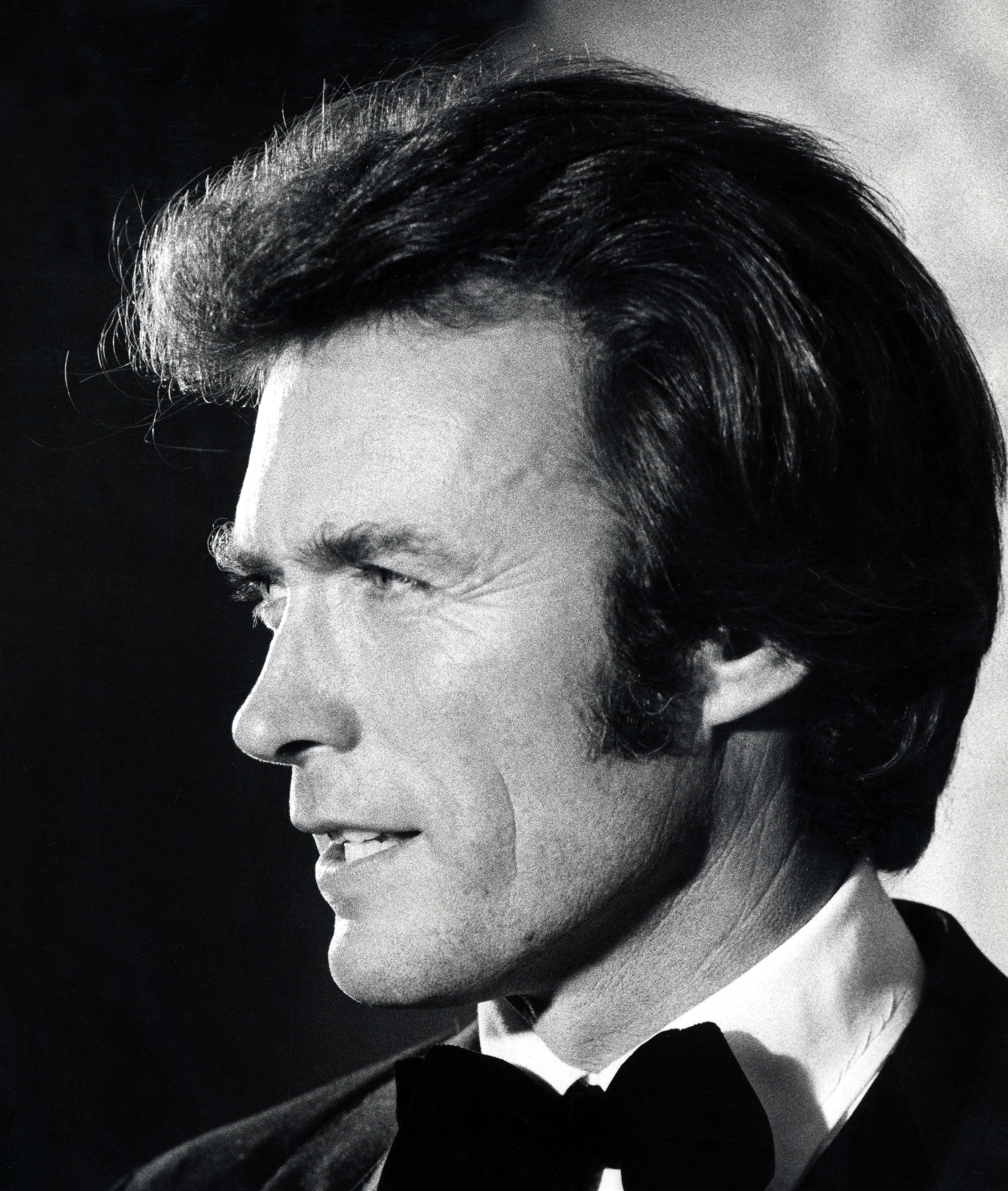 Clint Eastwood attended the National Association of Theatre Owners Awards at the Waldorf Astoria Hotel in New York City on October 28, 1971, dressed for the occasion in a classic black tuxedo, crisp white shirt, and oversized bow tie. The dramatic black-and-white profile portrait brought Clint's swept-back dark hair, pronounced brow, narrowed eyes, straight nose, and sharply defined jaw into focus