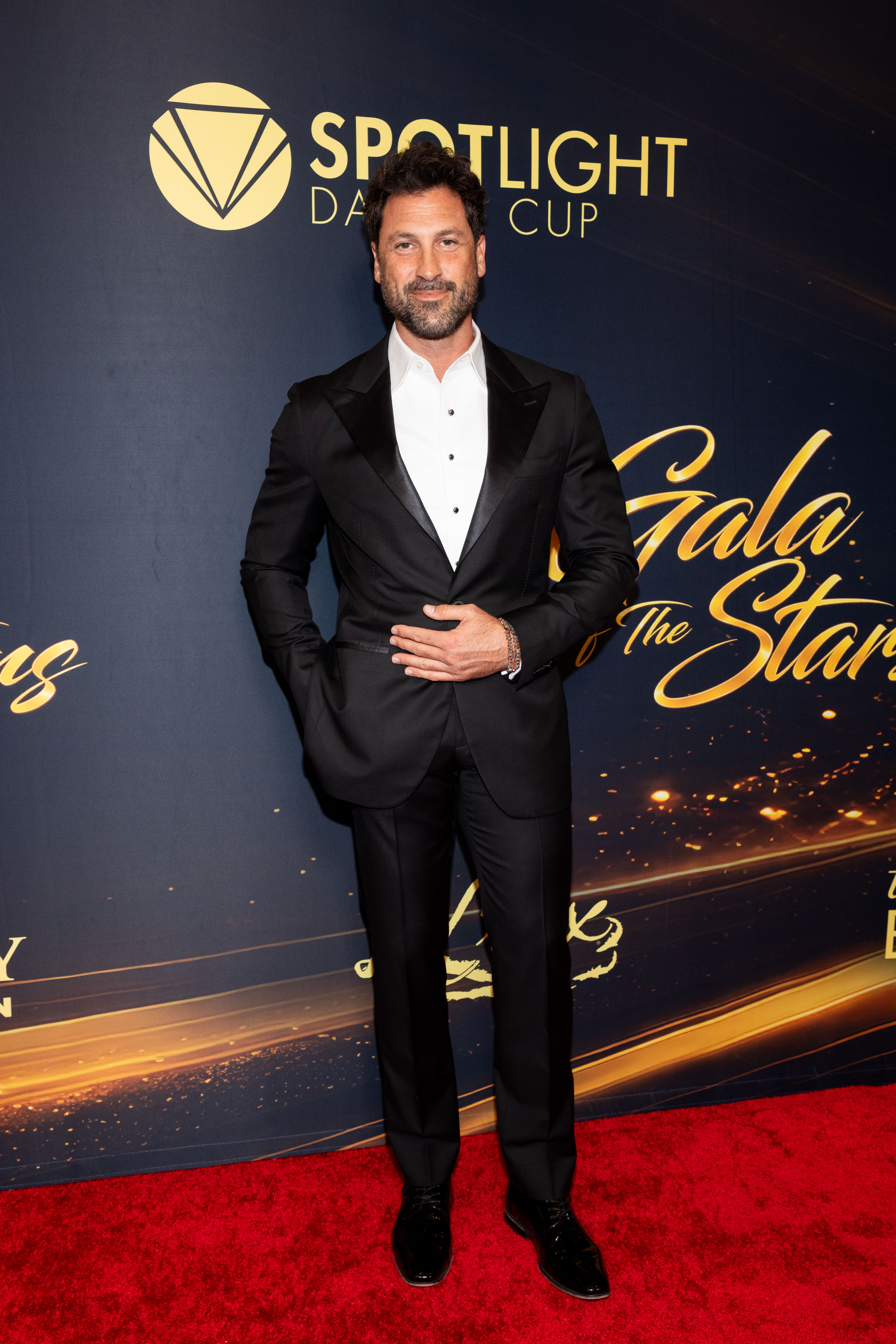 Maksim Chmerkovskiy poses on the red carpet in a black tuxedo with satin lapels, a white dress shirt, and polished black shoes at the 2026 Dancers Against Cancer Gala of the Stars. | Source: Getty Images