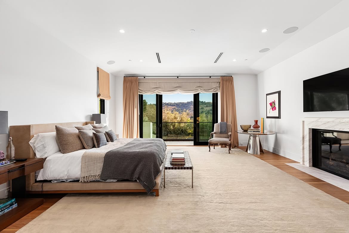 The spacious primary bedroom pairs neutral furnishings with a fireplace and broad glass doors overlooking the landscape. Its restrained decor leaves much of the floor open and puts the hillside view at the center of the room. | Source: Instagram/tomer.fridman