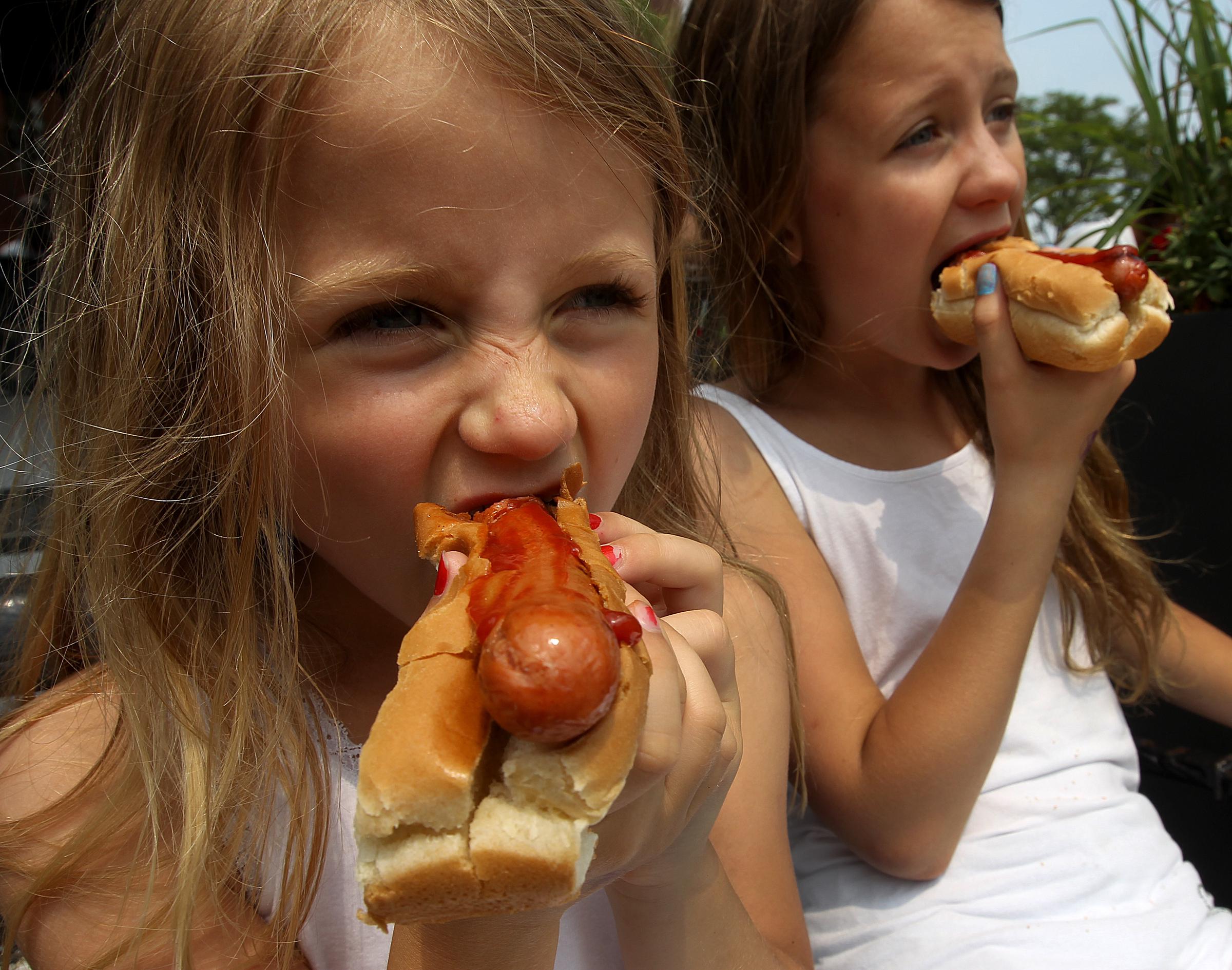 Two girls eat hot dogs topped with ketchup, highlighting the popular food at the center of Kayem Foods' latest recall. | Source: Getty Images
