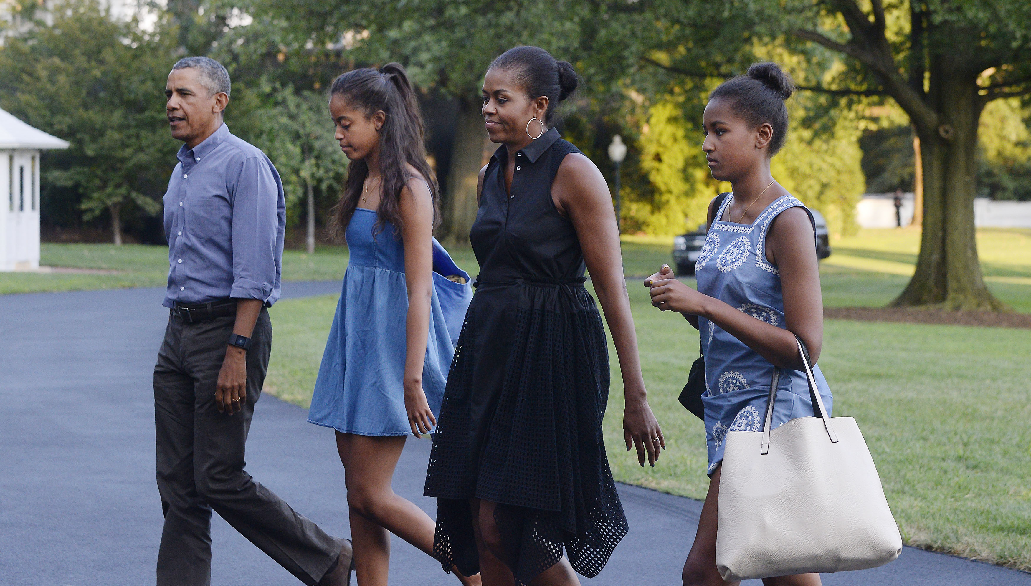 On August 23, 2015, in Washington, D.C., the Obamas returned from Martha’s Vineyard. Sasha, in a blue printed dress, walked the South Lawn beside Malia in denim, Michelle in black, and Barack in a button-down and slacks.