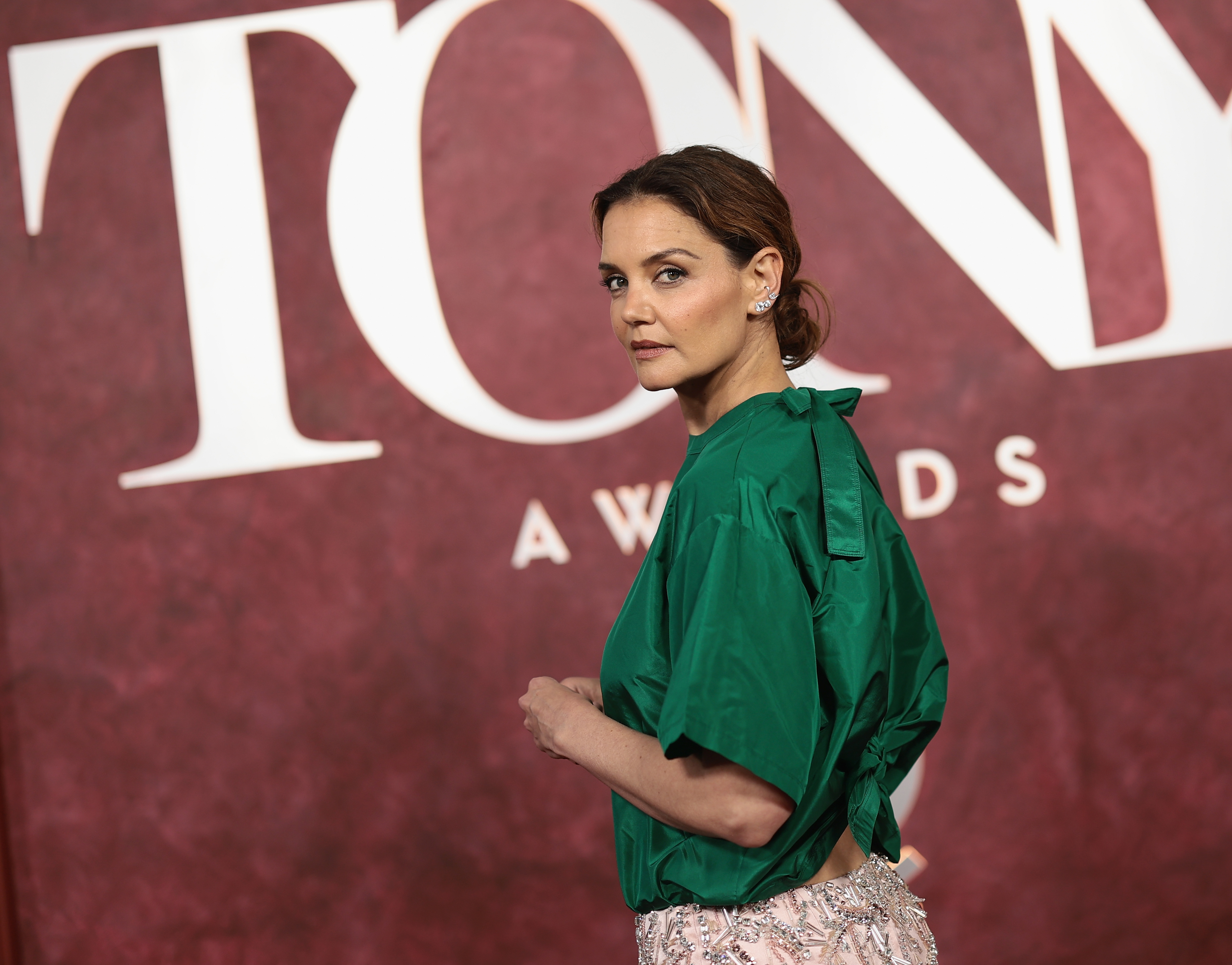 The actress turns heads in a vibrant emerald green top and pale pink beaded skirt during her arrival at the 78th Tony Awards, opting for a minimalist yet standout look against the event's deep red backdrop.