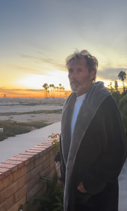 Against a sunset sky, Duguay stands near the beach wearing a dark robe. Thomas said he had returned to Florida to continue his care after recent appointments showed an improvement in his medical numbers. | Source: Instagram/mrs__shay