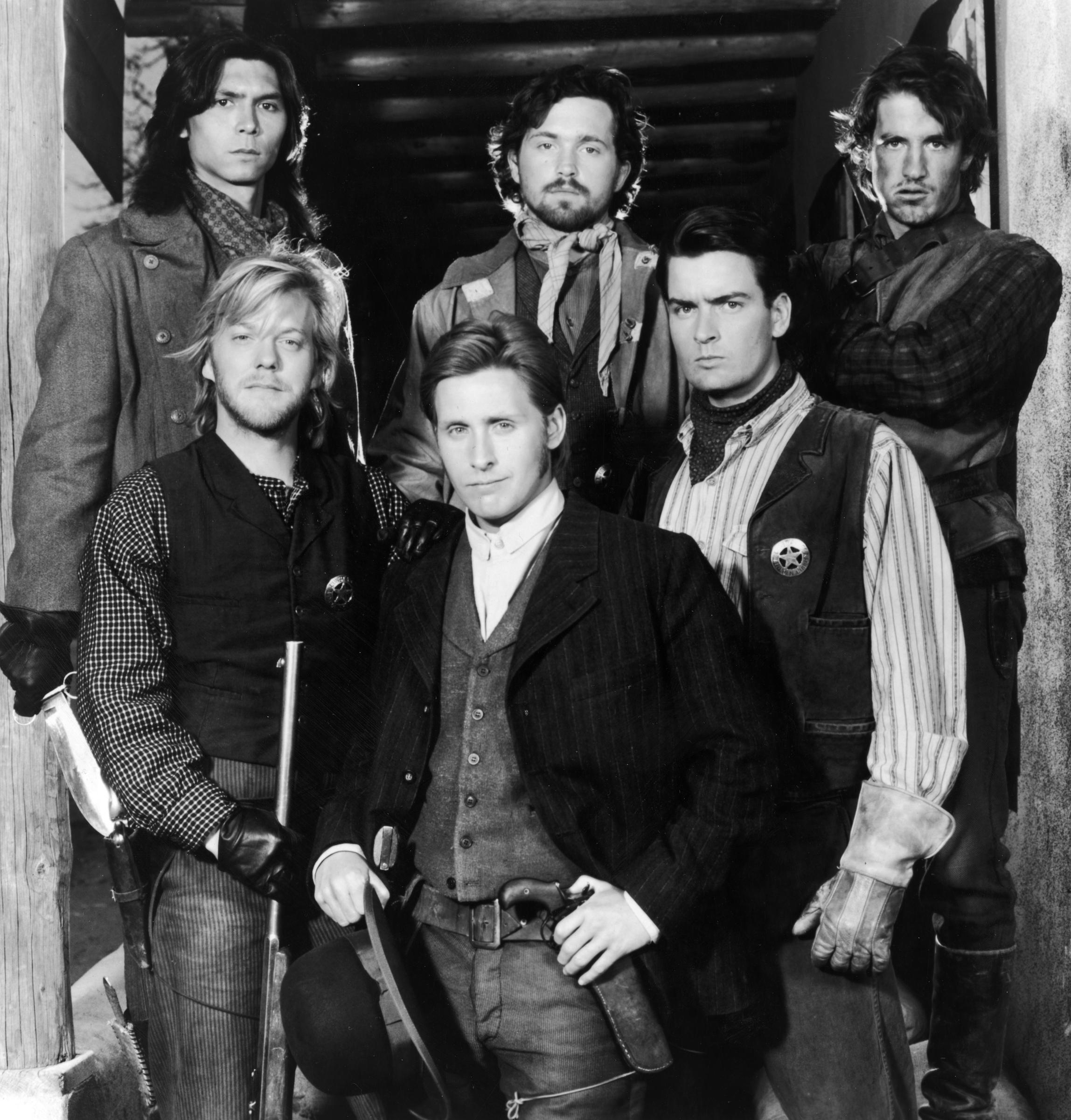 1988: Promotional portrait of the cast of the film Young Guns, directed by Christopher Cain. Lou Diamond Phillips, Dermot Mulroney, and Kiefer Sutherland stand in the back row, while Casey Siemaszko, Emilio Estevez, and Charlie Sheen pose in front, all dressed in period Western attire. | Source: Getty Images