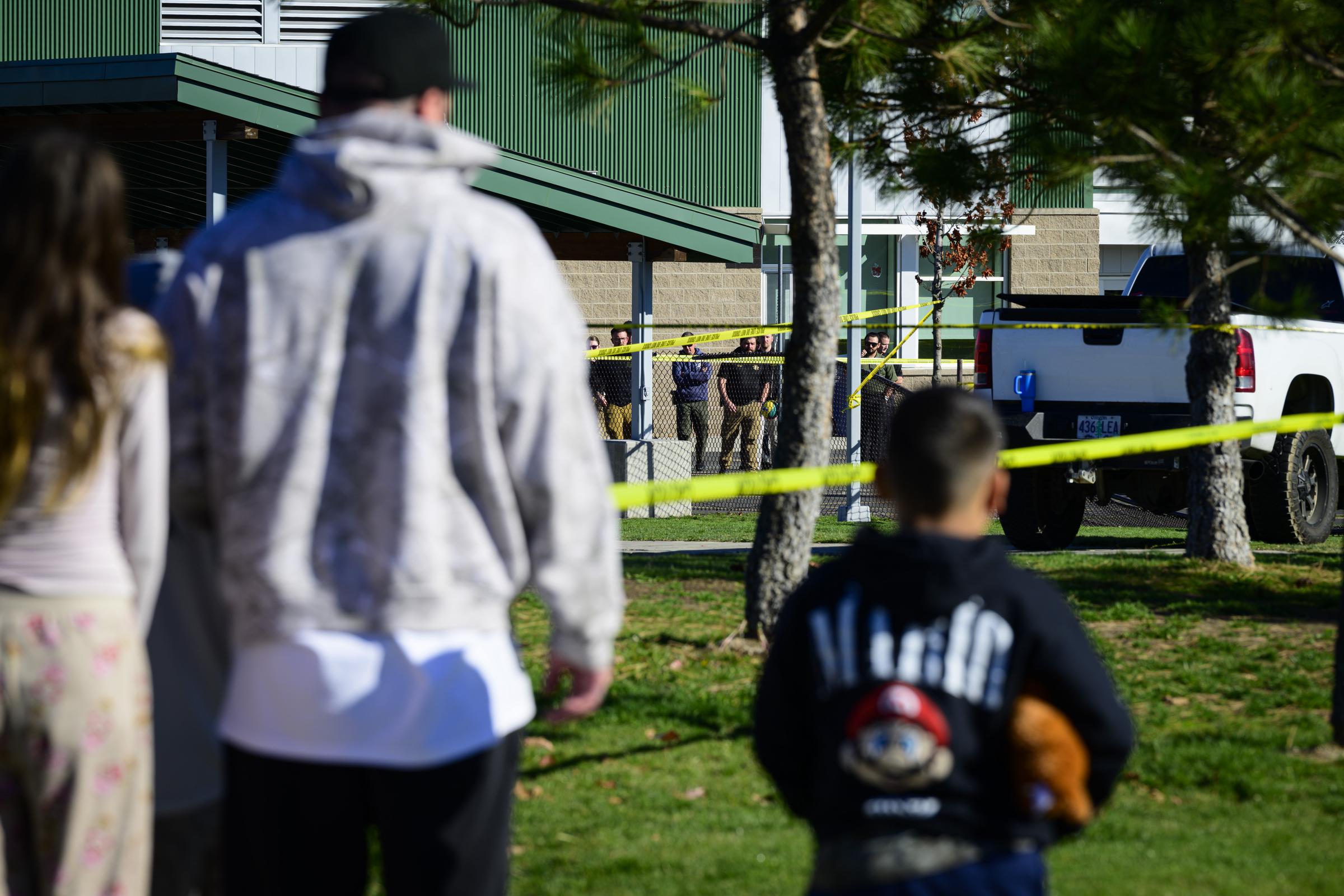 A child clutching a stuffed animal stands with adults outside Silver Rail Elementary as investigators work behind police tape following the deadly shooting. | Source: Getty Images.