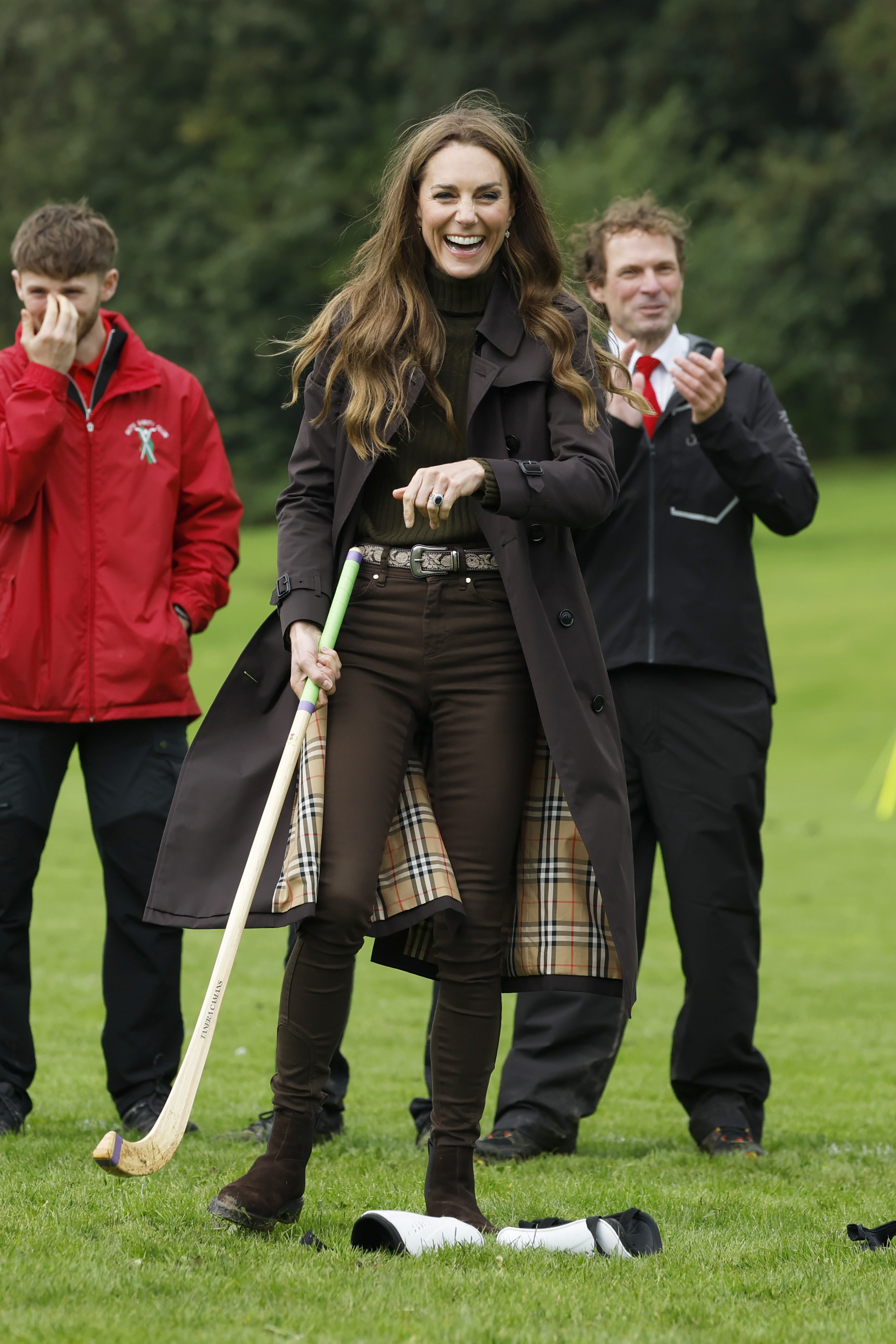 Catherine, Princess of Wales, smiles broadly as she holds the caman on the shinty pitch, with players and onlookers gathered behind her during the royal visit. | Source: Getty Images