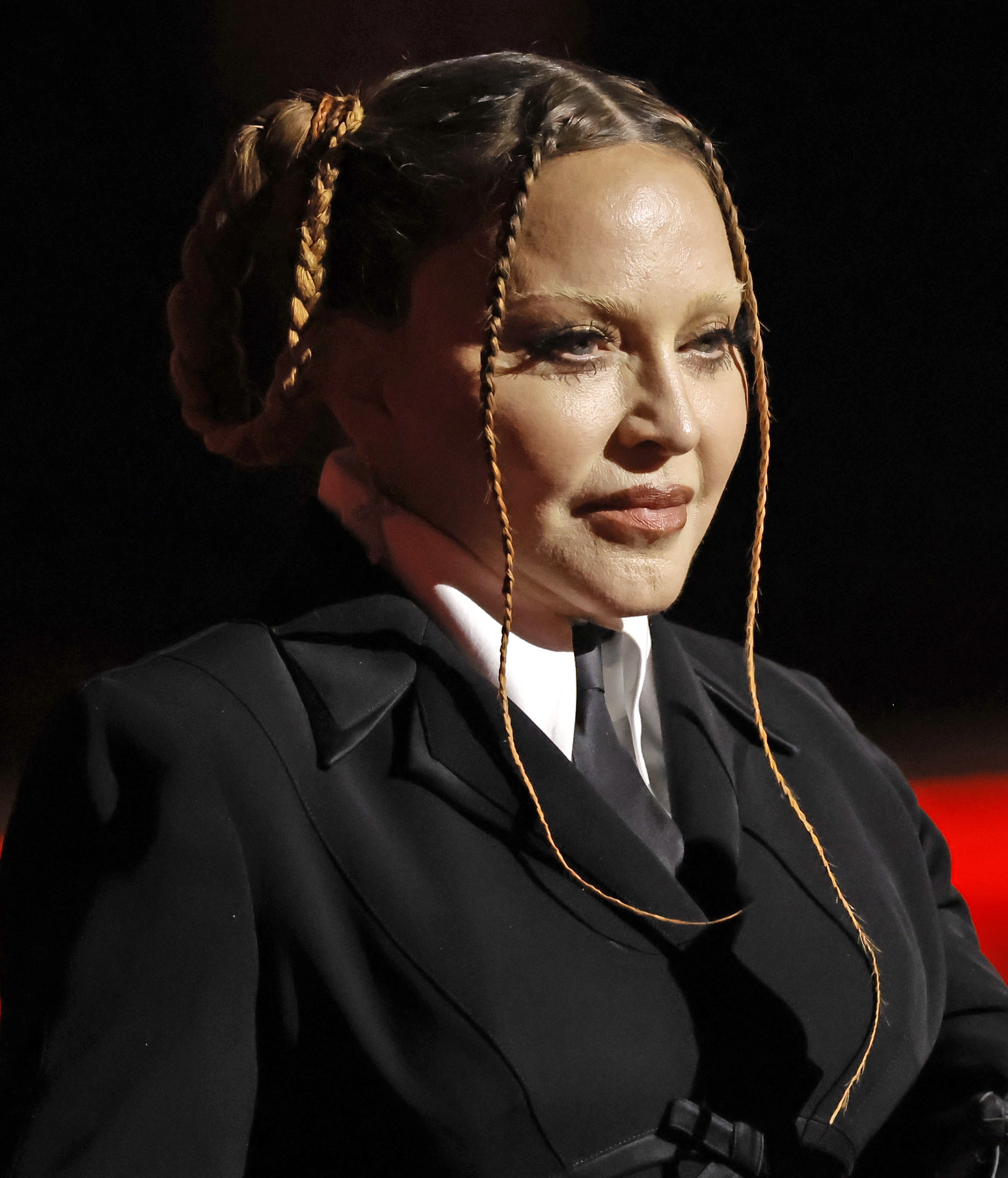 Madonna is pictured in a sharply tailored black suit and tie, with her hair swept back and thin braids framing her face. | Source: Chat GPT