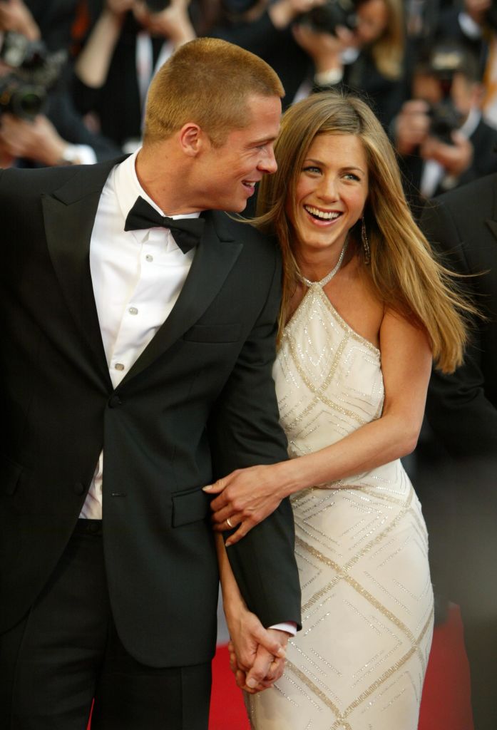 Looking radiant in a white halter gown with sparkling details on the red carpet, Jennifer Aniston holds hands with Brad Pitt. She beams with laughter and joy, exuding glamour and elegance.