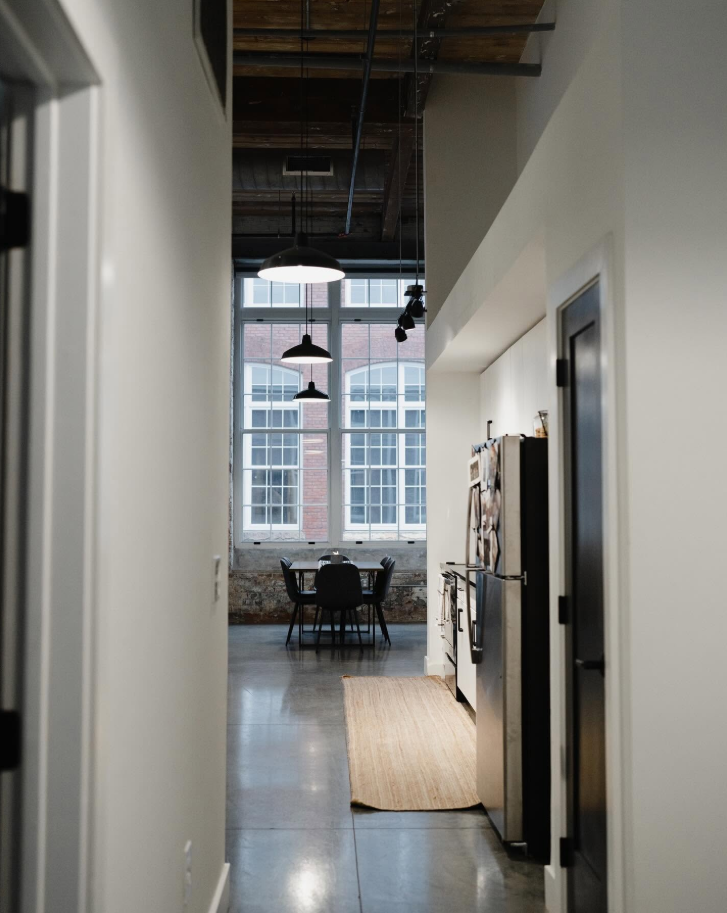A view from inside the loft highlights the apartment’s open layout, leading from the kitchen area toward the dining space and its oversized windows. | Source: Facebook/Judson Mills Loft