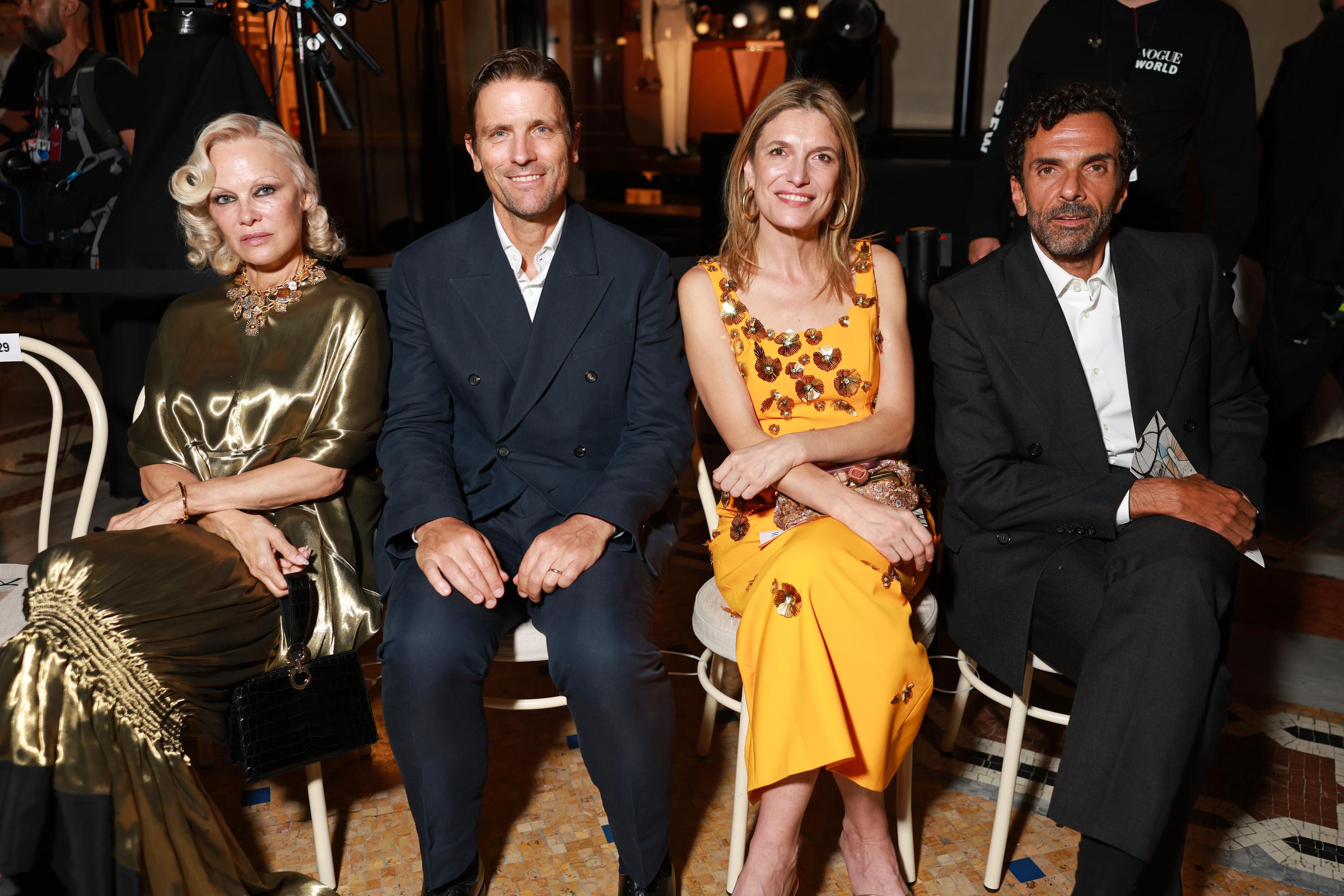 Pamela Anderson sits with fellow attendees at Vogue World: Milano 2026 at Galleria Vittorio Emanuele II on September 22, 2026. Her metallic gold gown, statement necklace and smoky eye remained on display inside the Milan venue. | Source: Getty Images