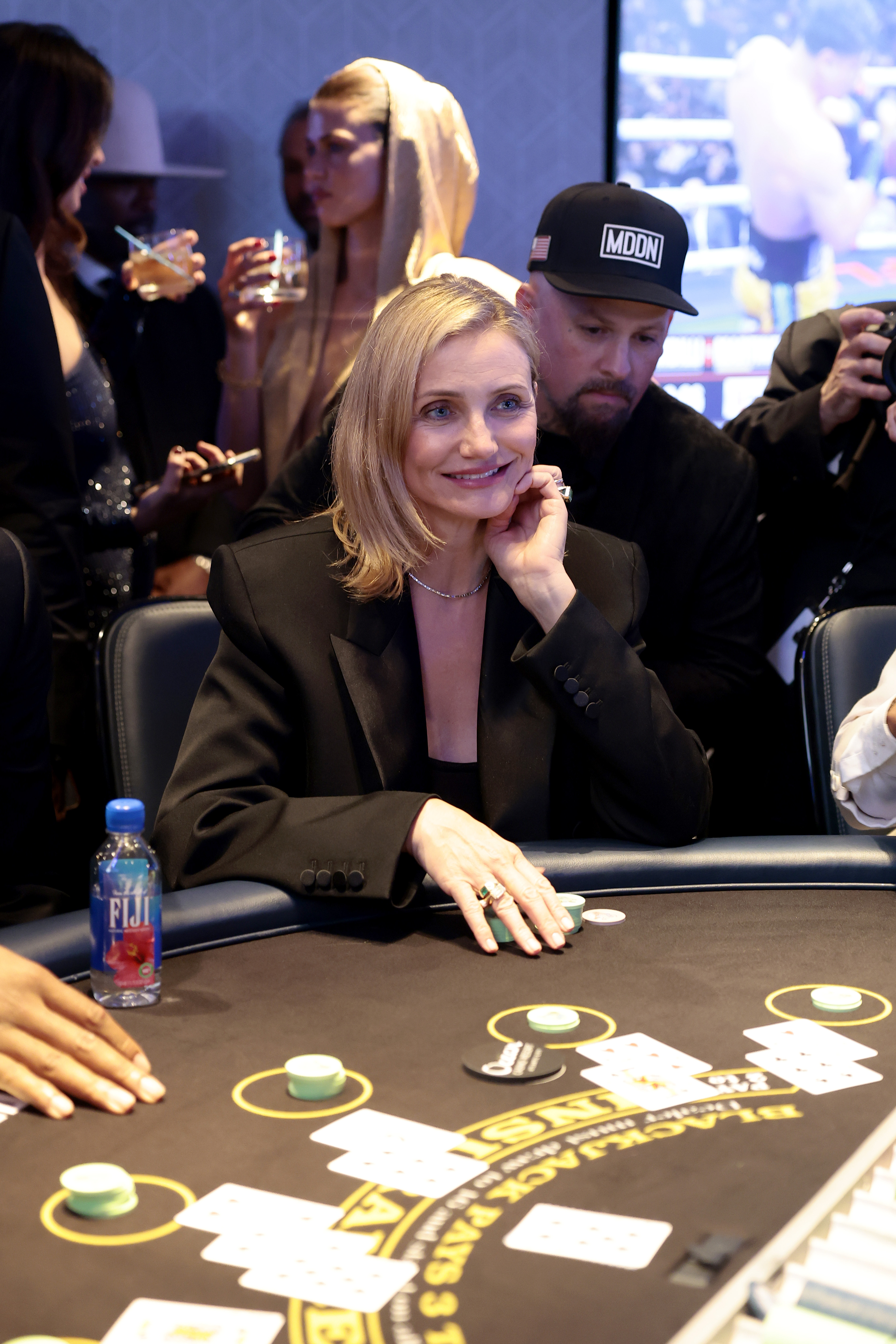 During the event, Cameron Diaz was photographed at the blackjack table, smiling as she leaned on her hand with a stack of chips in front of her. Dressed in a sharp black blazer and simple jewelry, the actress exuded relaxed confidence while her husband stood just behind her, watching the action unfold.