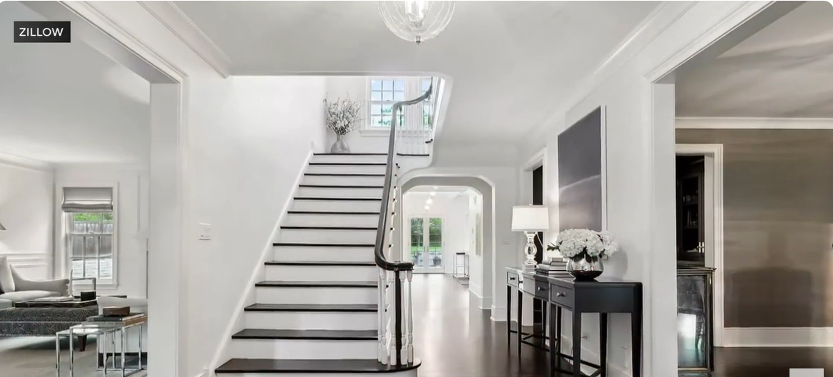 The iconic "Home Alone" staircase has been transformed into a sleek, modern entryway featuring crisp white walls, dark wood floors, and a polished black handrail. A bright window at the top floods the space with natural light, highlighting the elegant simplicity. The updated design blends timeless charm with contemporary sophistication. | Source: YouTube/ CBSChicago