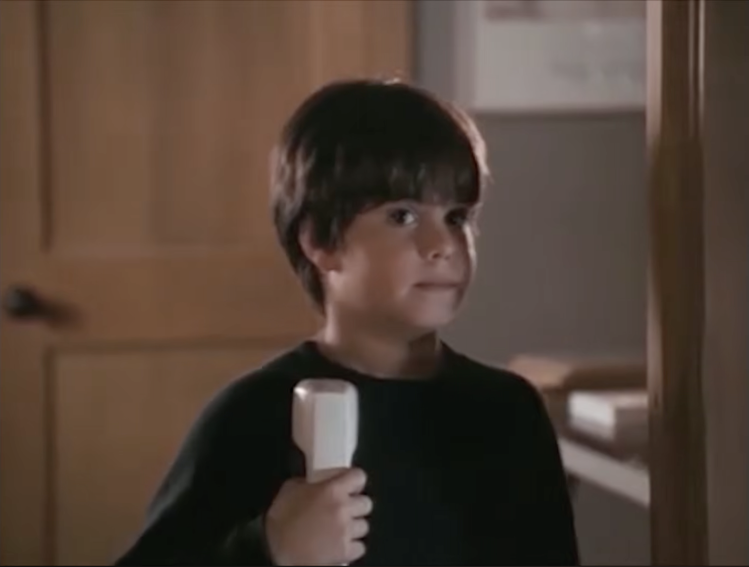 The young boy holds a telephone and gives a mischievous sideways glance in a scene from Sleepless in Seattle, showing the playful personality that made his character so memorable. | Source: Rotten Tomatoes Classic Trailers / YouTube.
