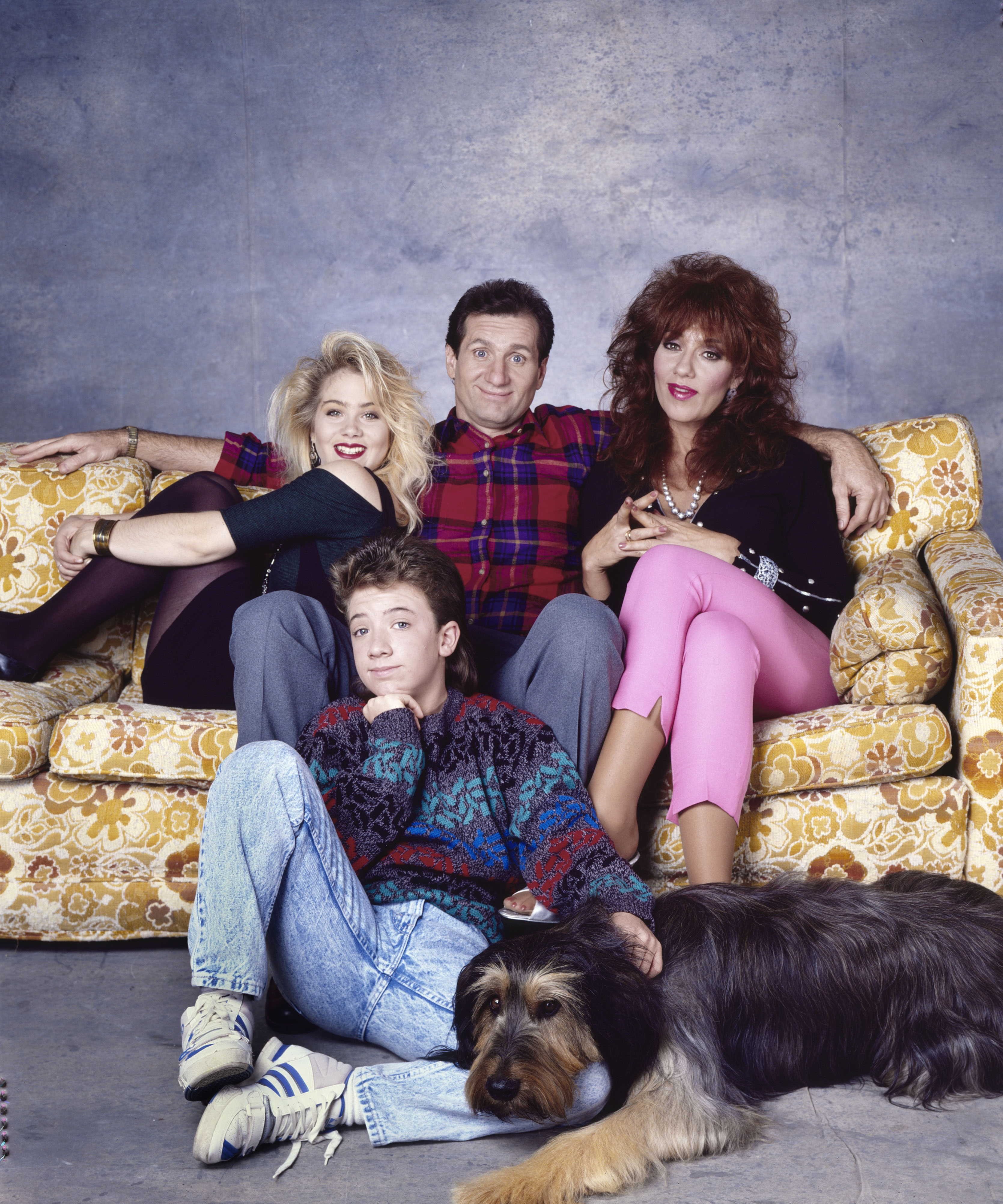 Christina Applegate, David Faustino, Ed O'Neill, and Katey Sagal struck a quintessential Bundy family pose alongside their shaggy Briard, Buck, during a promotional photoshoot for "Married... with Children" in October 1988 in Los Angeles, California. Draped over their floral living room sofa in full character attire—ranging from Kelly's teased blonde hair to Peggy's bright pink capris and Al's plaid flannel—the ensemble radiated the irreverent, dysfunctional charm that turned the sitcom into a television sensation. | Source: Getty Images