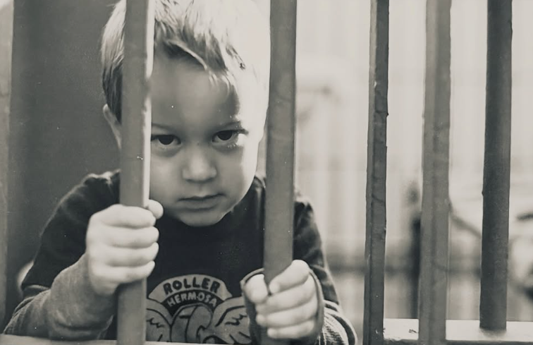 Deacon grips the bars in another close-up childhood portrait, staring directly at the camera. The black-and-white photograph captures a more serious expression from his early years. | Source: Instagram/Deaconphillippe