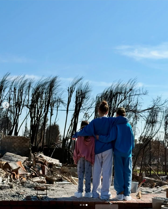 Fiona and her sisters stand together among the ruins of their family home after the devastating fire, their arms around one another. The photograph captures the siblings facing what was left behind while holding onto the one thing their father said they still had: each other. | Source: Instagram/ichadlowe