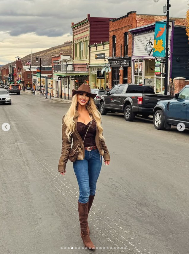 Jennifer Eckhart smiles for the camera while walking through a picturesque downtown street, wearing a brown leather jacket, cowboy hat, jeans and knee-high boots. | Source: Instagram/jennifereckhart
