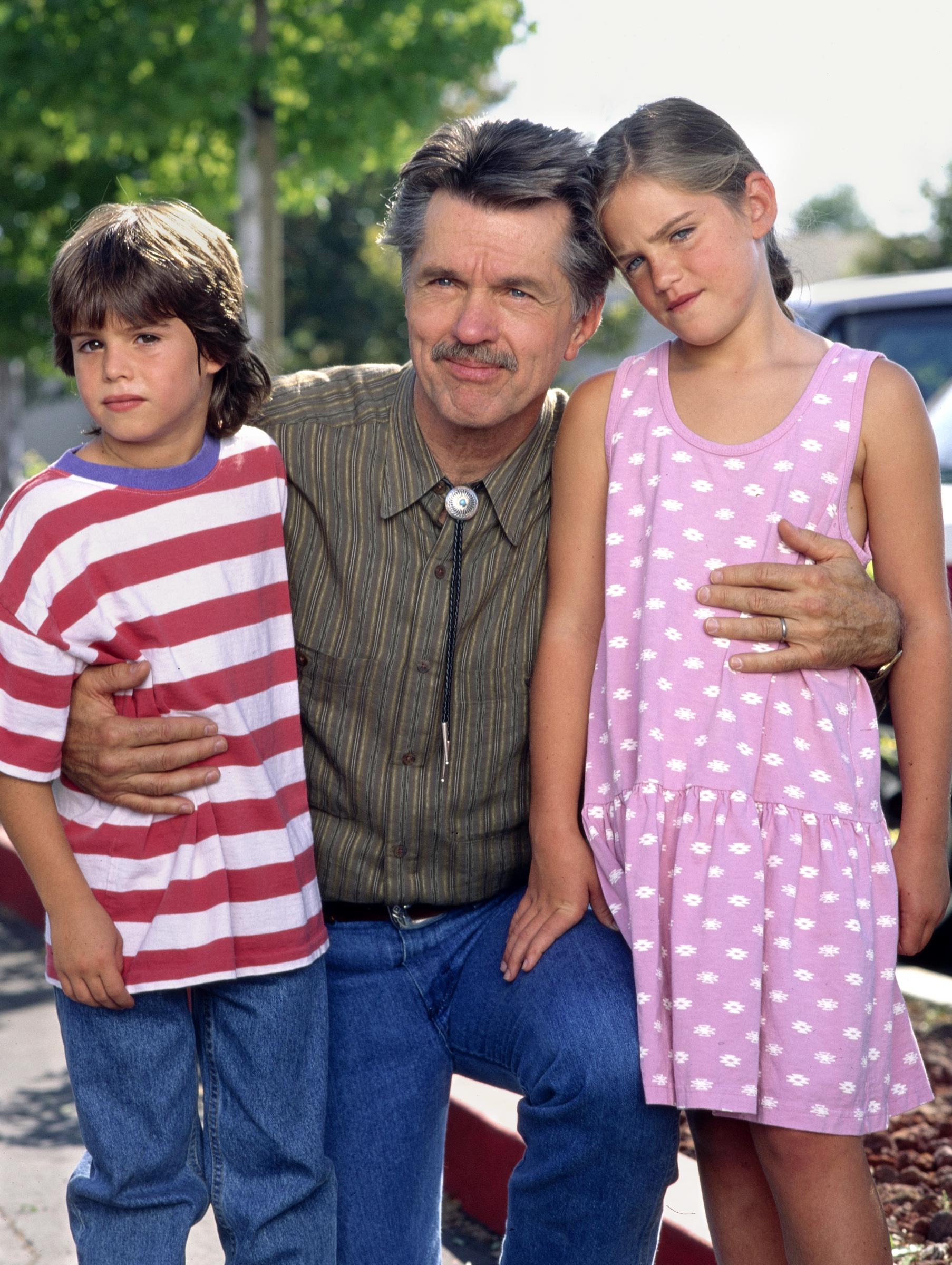 Ross Malinger poses alongside an older man and a young girl in an archival photograph, wearing a red-and-white striped shirt — a glimpse of his early years as a child actor. | Source: Getty Images.