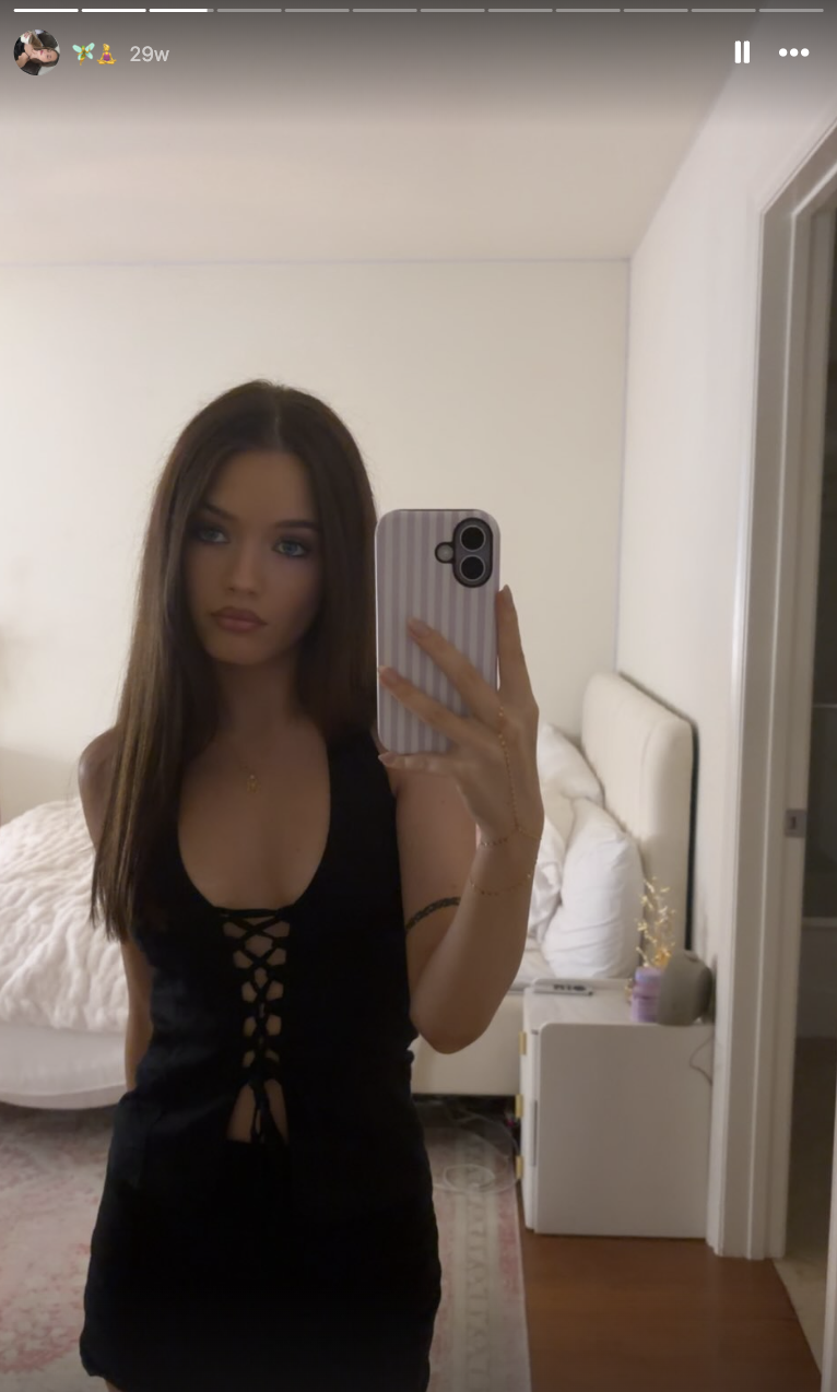 Harper Lockwood snaps a bedroom mirror selfie wearing a lace-up black halter top with her long brunette hair styled straight and parted in the center.