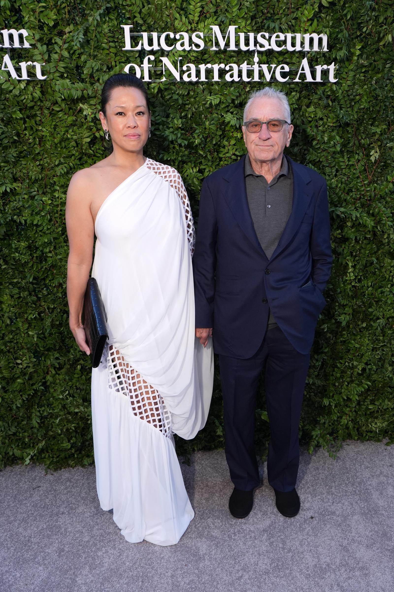 Tiffany Chen's flowing white gown stood out beside Robert De Niro's darker ensemble as the pair posed together. Their appearance added another distinctive look to the evening. | Source: Getty Images